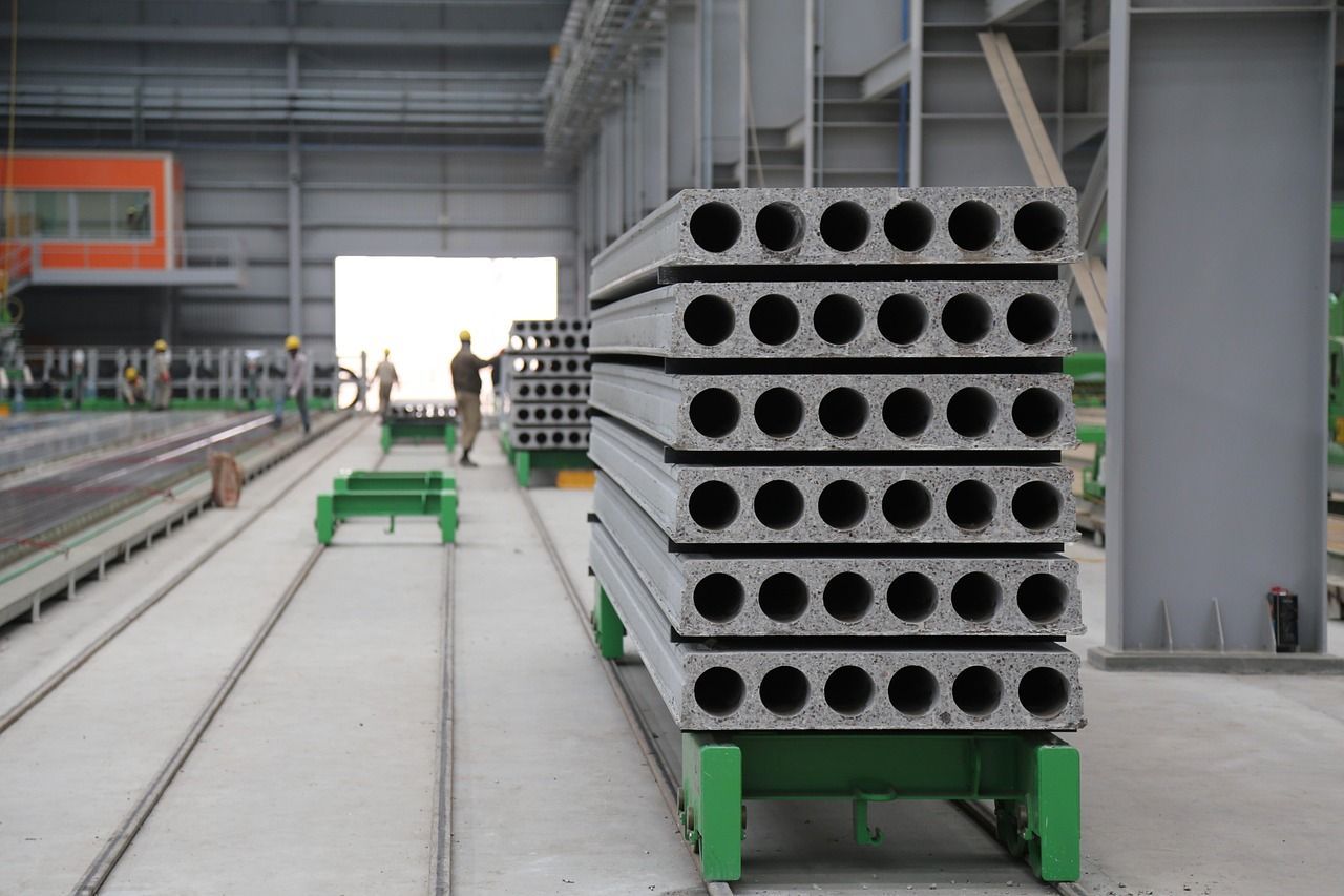 Stack of precast concrete slabs with circular voids, inside a factory setting.