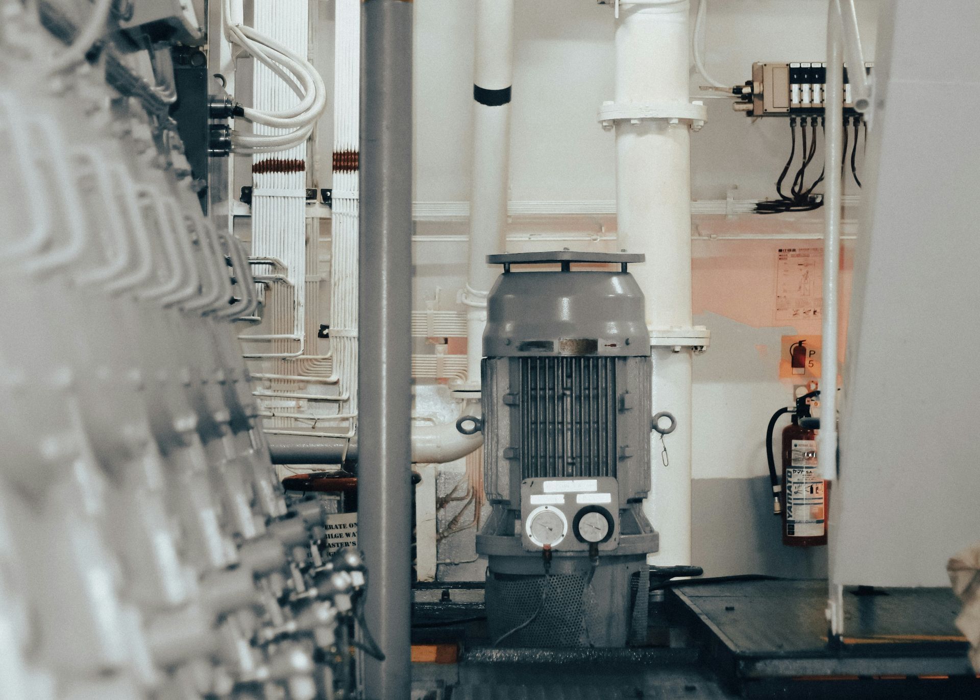 Industrial machinery in a utility room with pipes, wires, and a fire extinguisher.