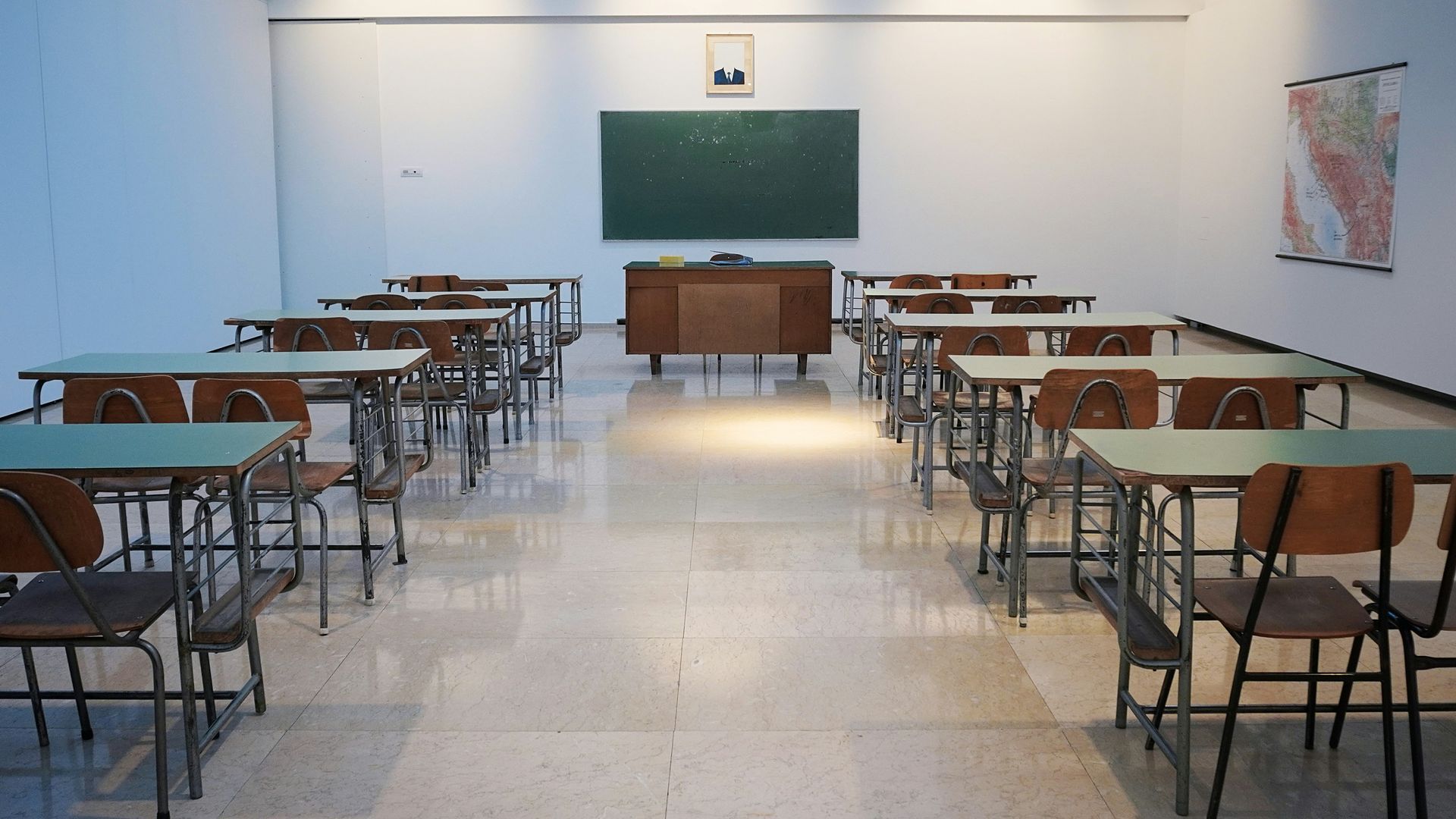 Empty classroom with rows of desks facing a chalkboard and teacher's desk.