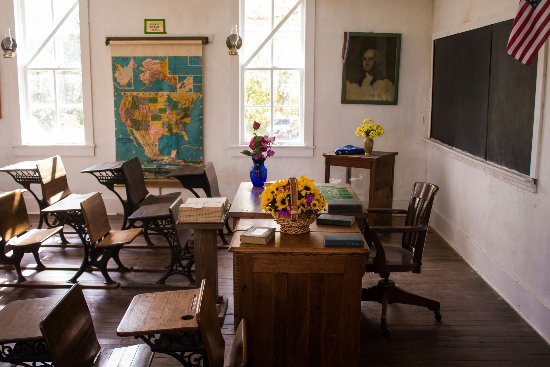 Vintage classroom with wooden desks, blackboard, and a world map. Sunlight streams through windows.