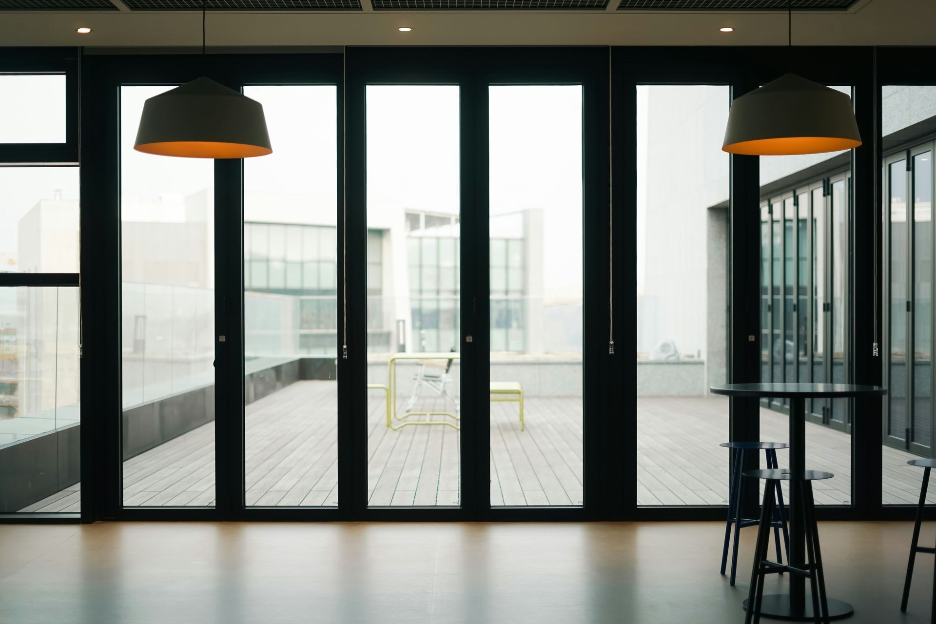 Modern interior with large glass doors leading to a balcony, two hanging lamps, a table, and chairs.