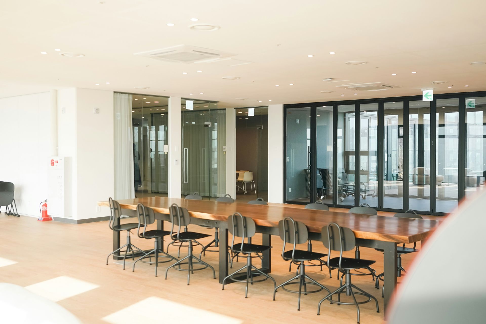 Spacious office with large wooden table and chairs, glass walls, and bright lighting.