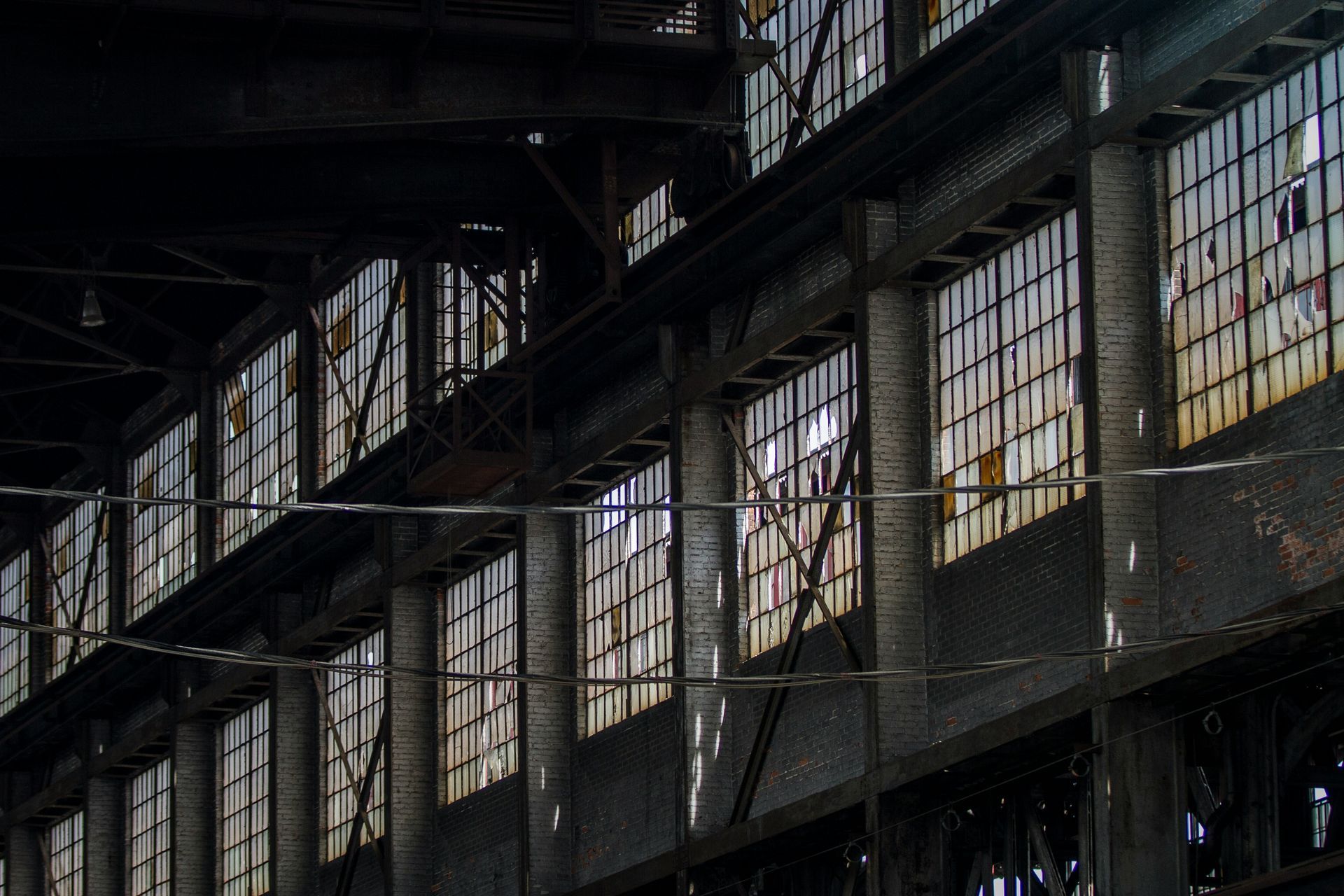 Interior view of an old industrial building with rows of rectangular windows, sunlight and shadows.
