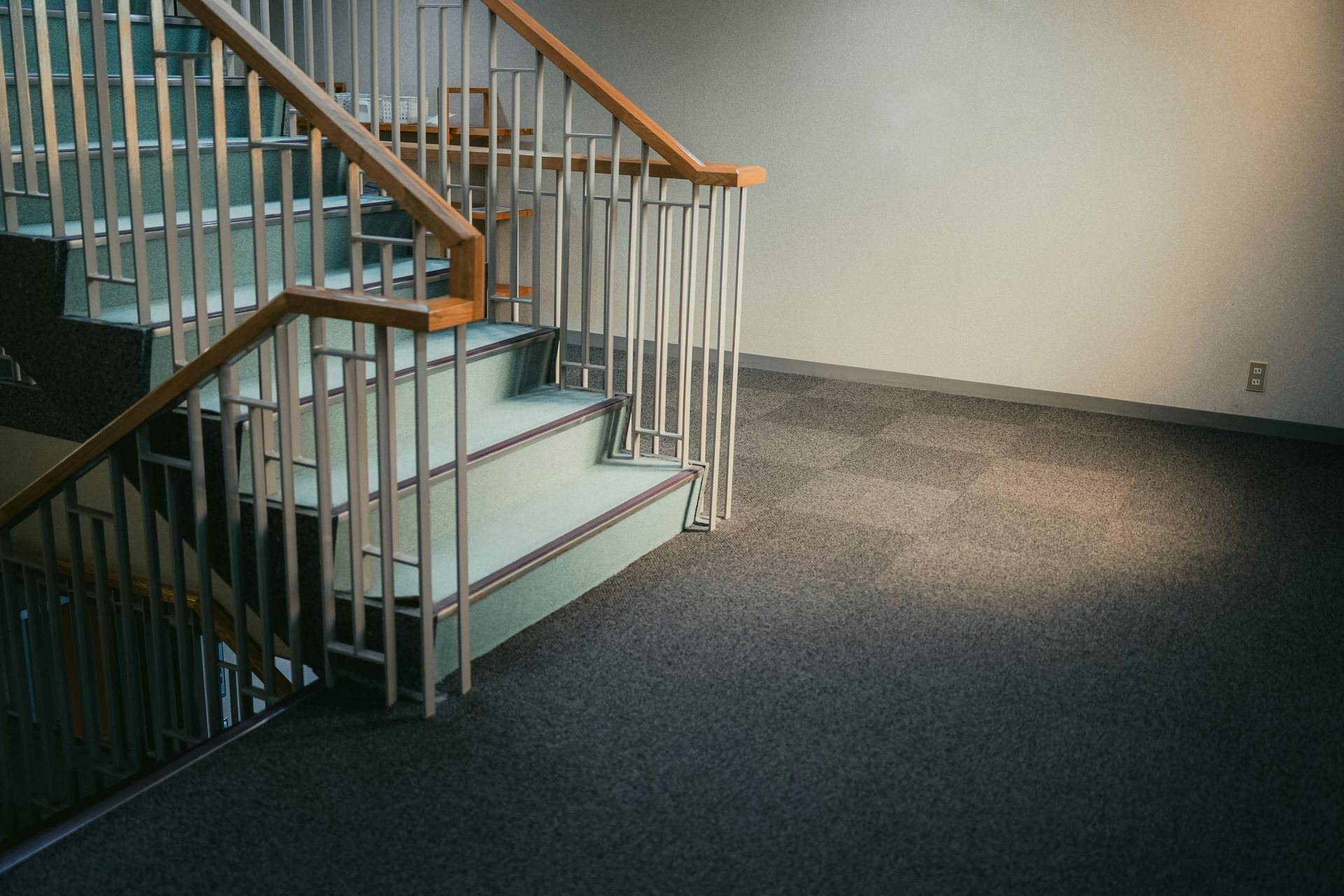 Staircase with light green steps, white railing, wooden handrails, and dark carpet.