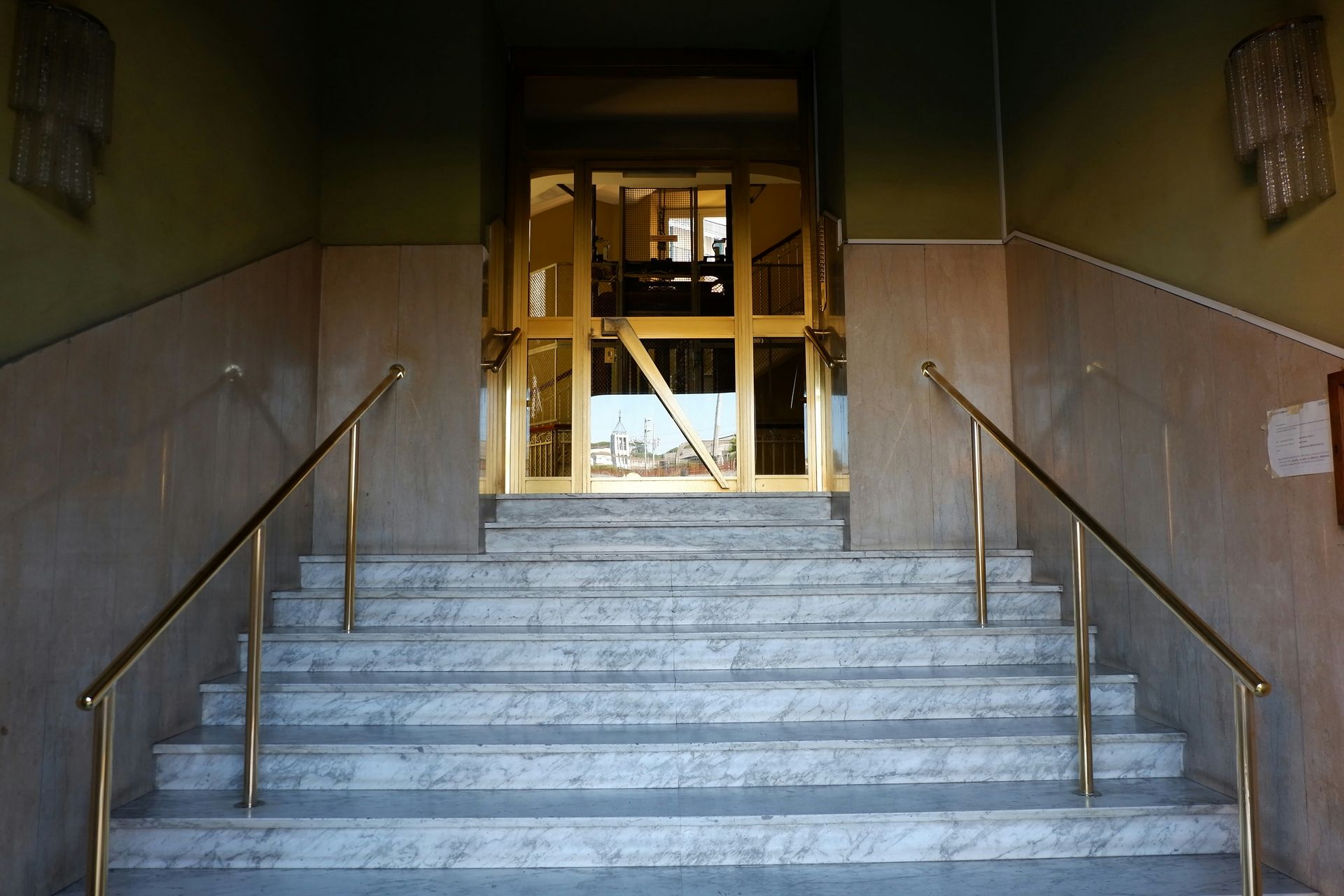 Steps leading up to a gold door in a building. Handrails are on either side.