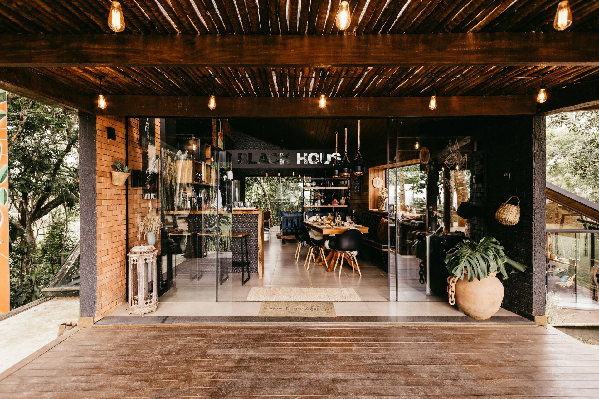 Entrance to a restaurant, glass doors, wooden porch, string lights, interior dining area visible.