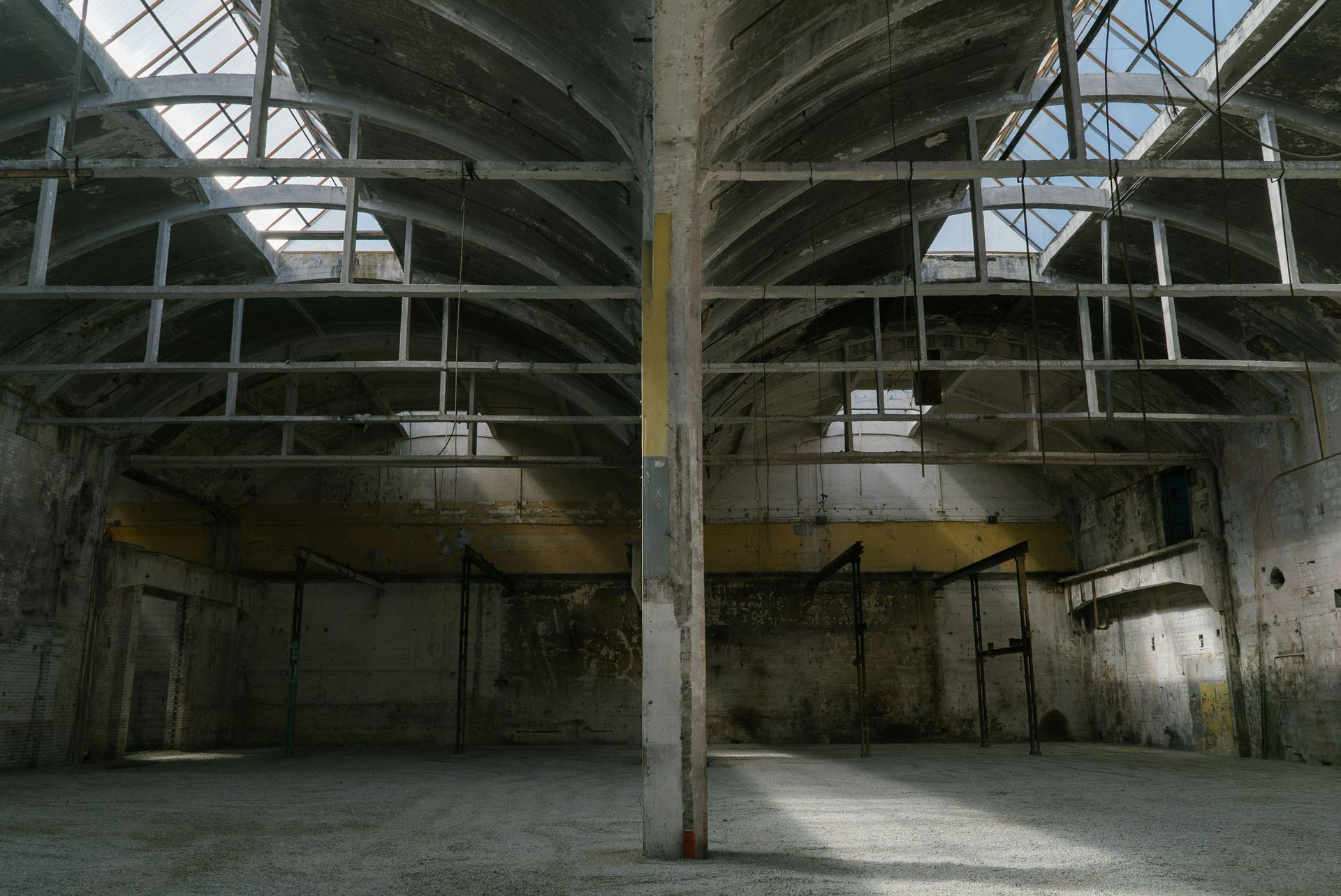 An abandoned, decaying industrial interior with a high ceiling and skylights.