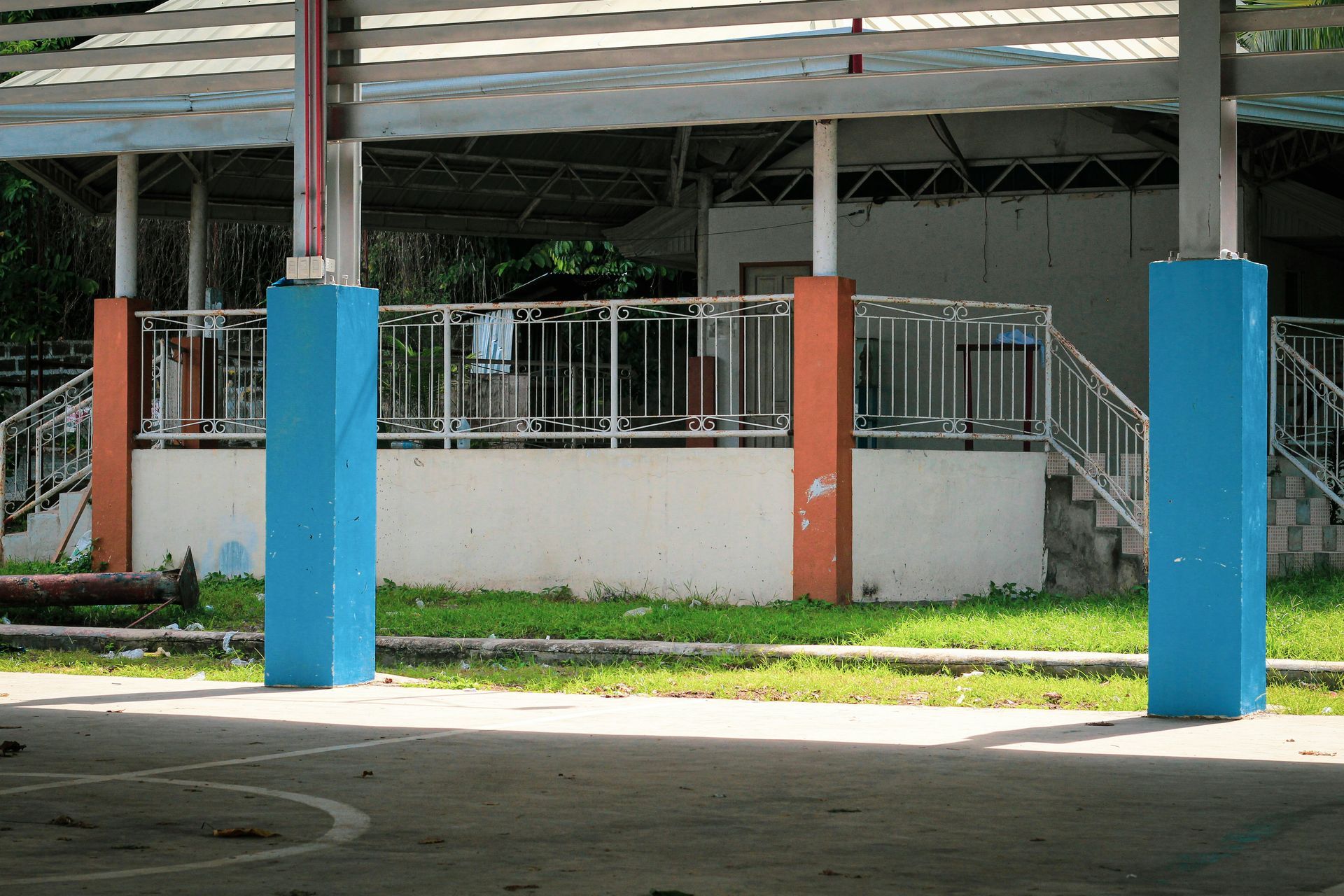 Two blue support pillars on a concrete surface, in front of a building with a white railing.