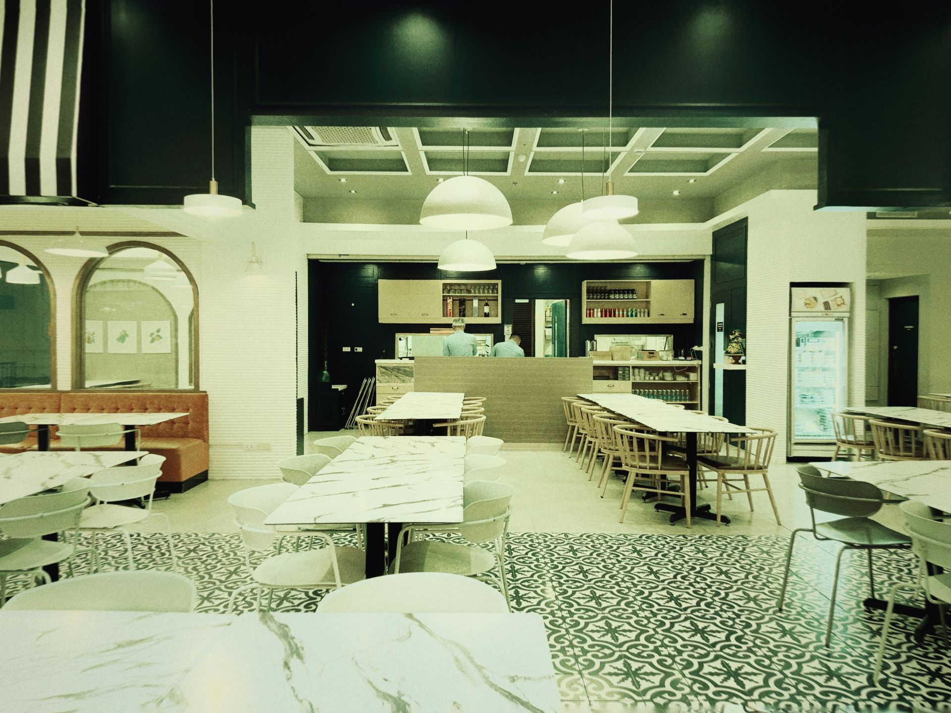 Interior view of a modern restaurant with tables, chairs, and a counter. The floor has a black and white pattern.