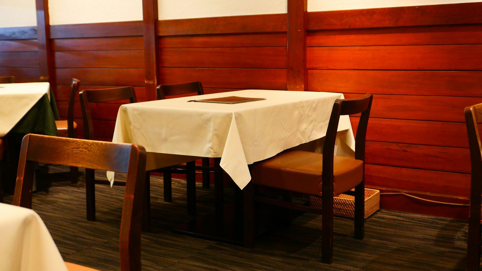 Dining room with square table draped in a white cloth, wooden chairs, and dark wood paneling on the walls.