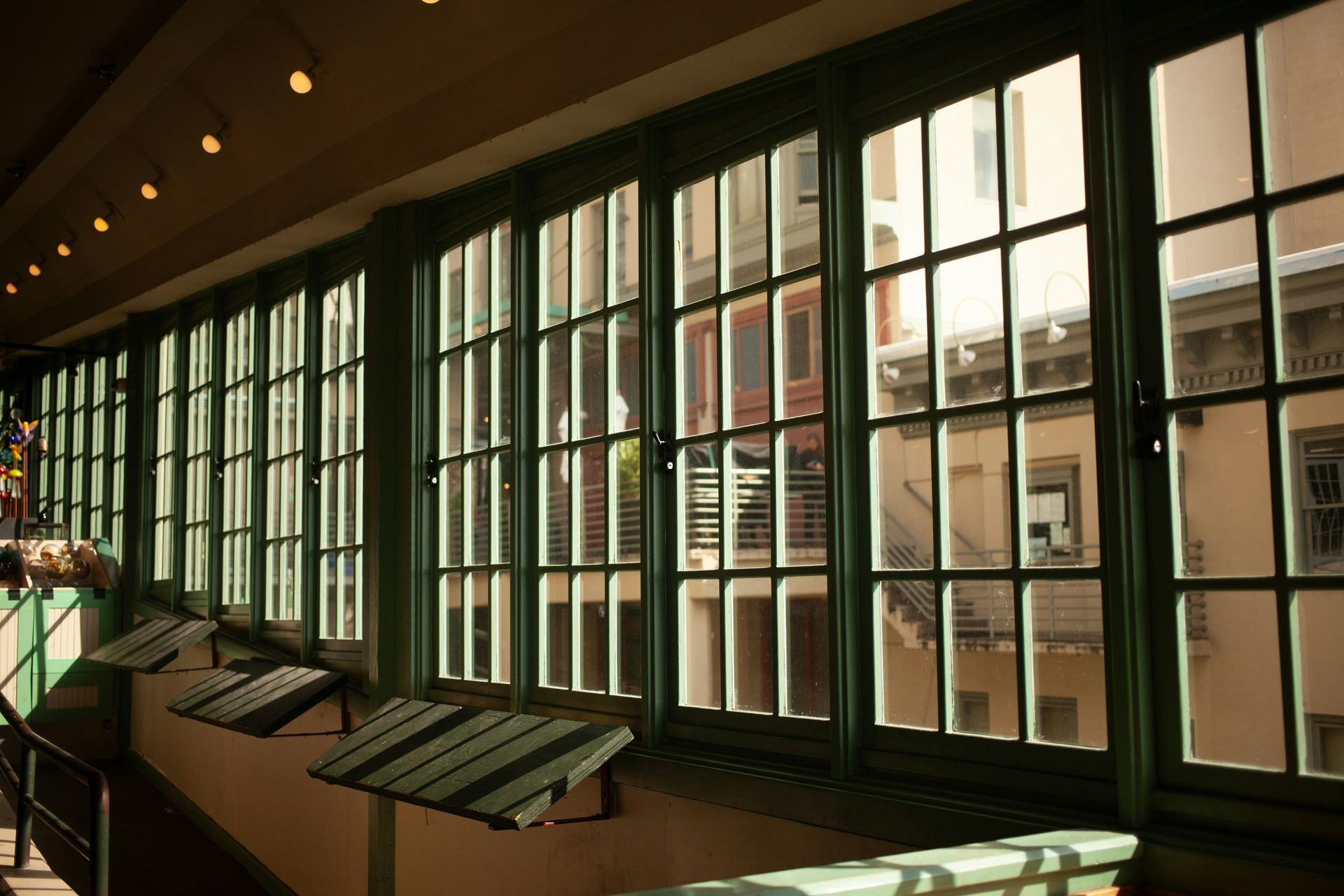 Row of green-framed windows looking out onto a building courtyard, interior, sunny.
