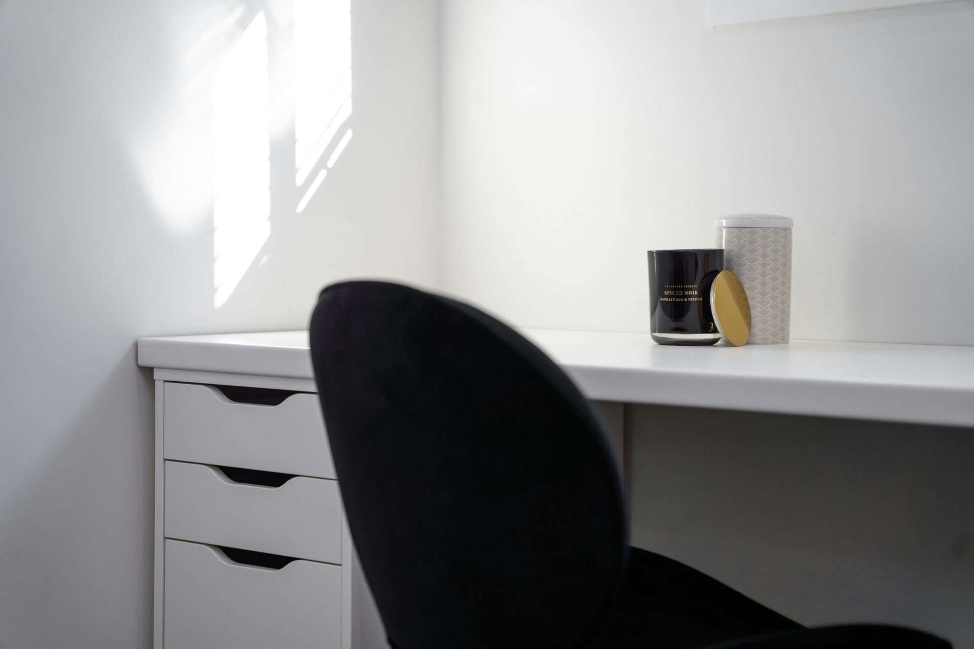 White desk with black chair. Three decorative items on desk. Sunlight streaming in.