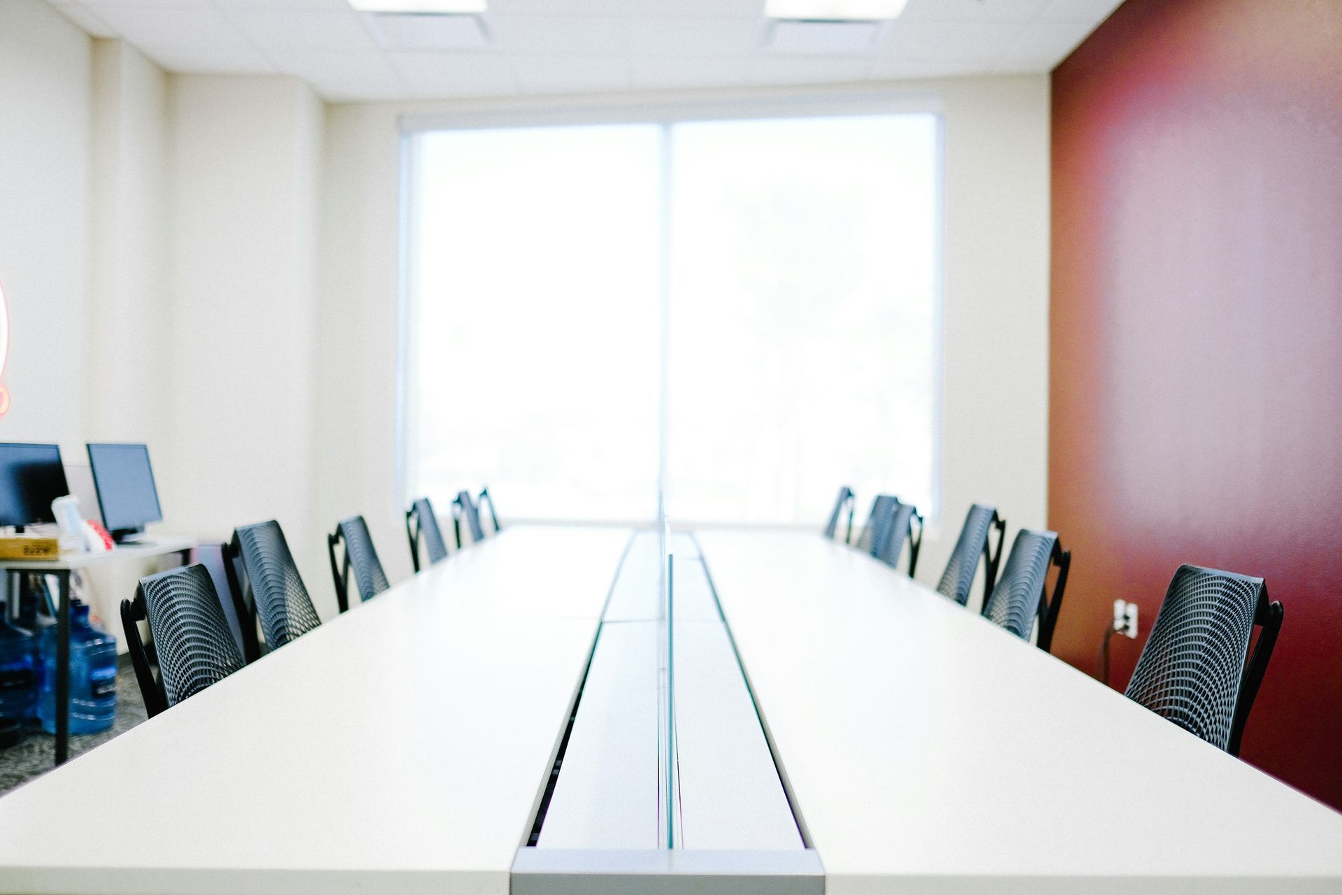 Empty conference room with long table, chairs, and large windows. Red accent wall.