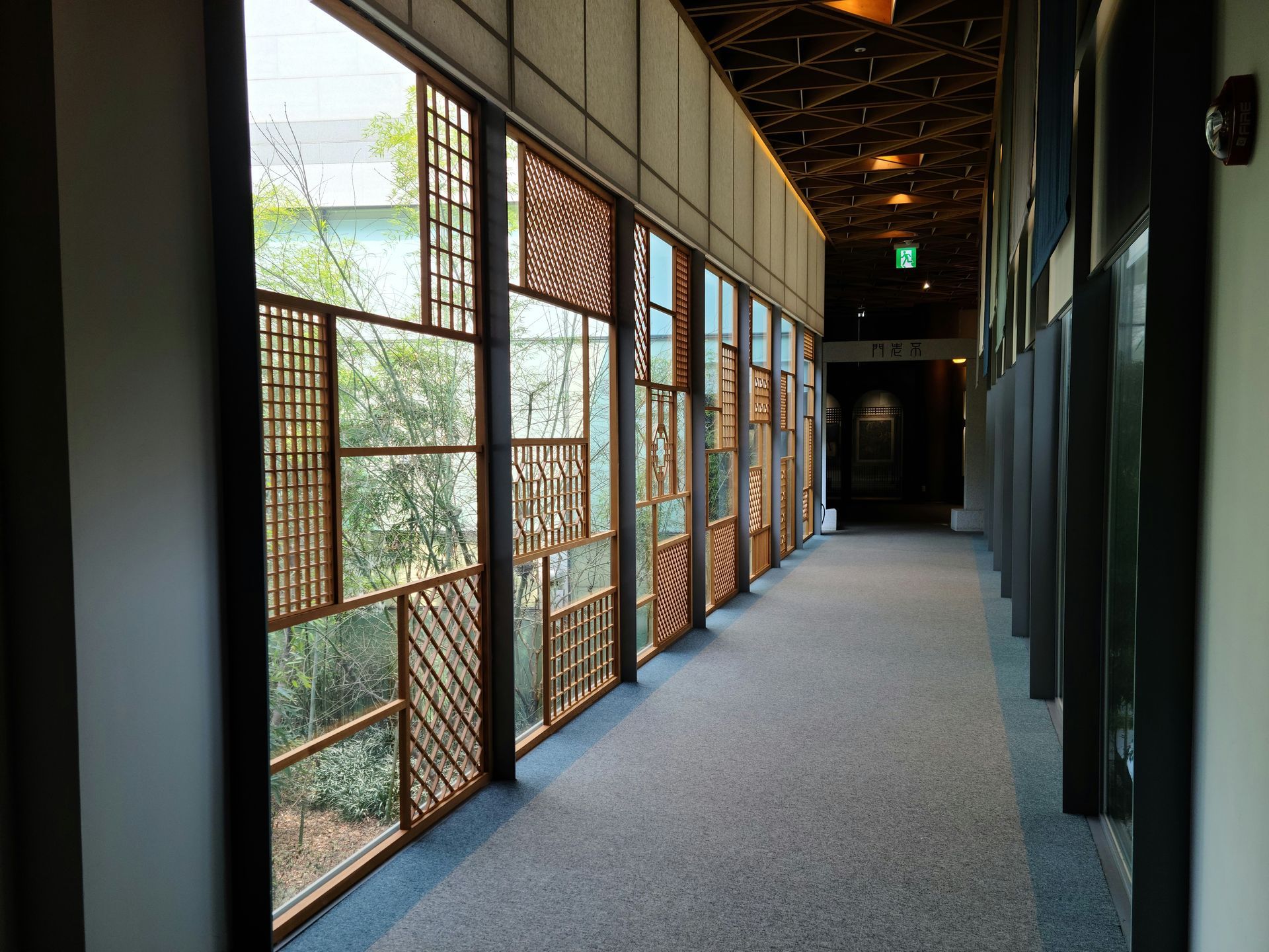 Long hallway with patterned wooden window panels and a blue carpet.