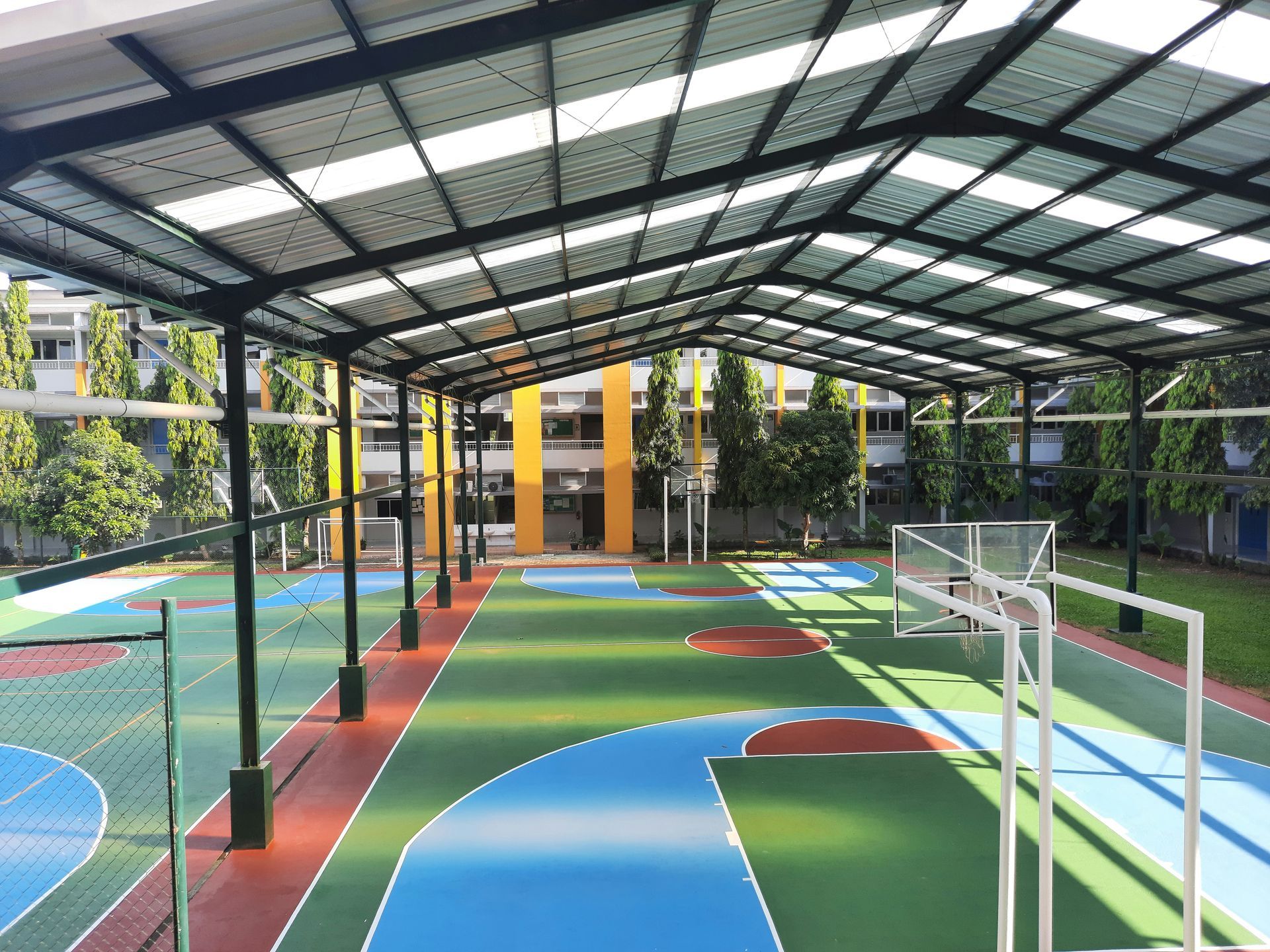 Covered outdoor sports court with basketball hoops and colorful playing surfaces.