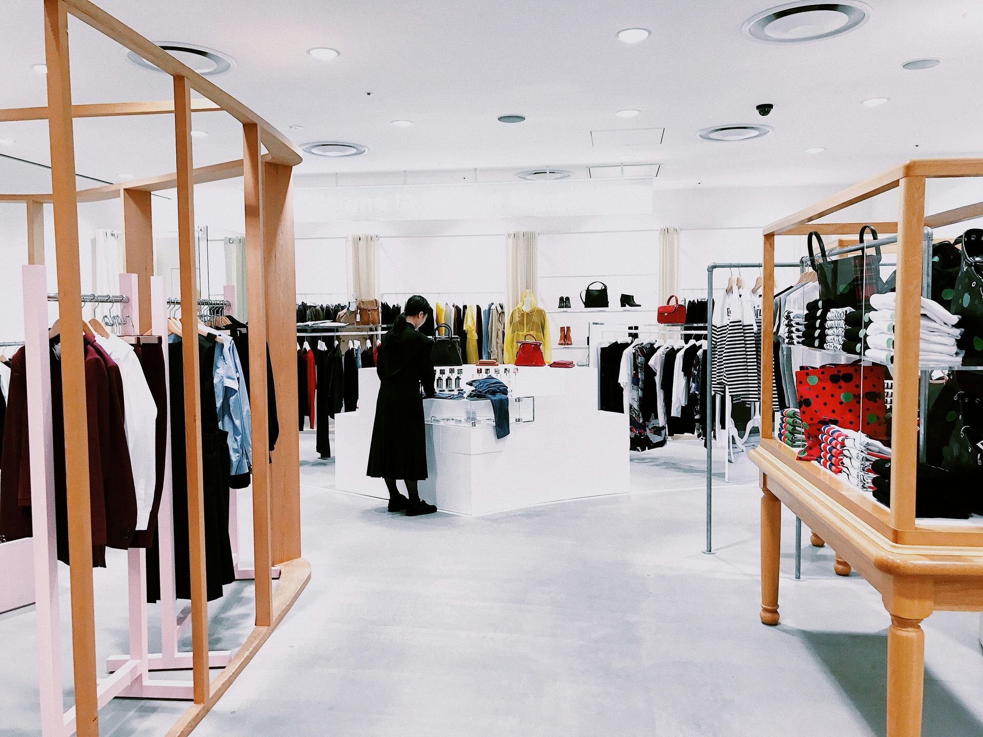 A person shopping in a brightly lit clothing store. Racks of clothes are visible with light wood and pink shelving.