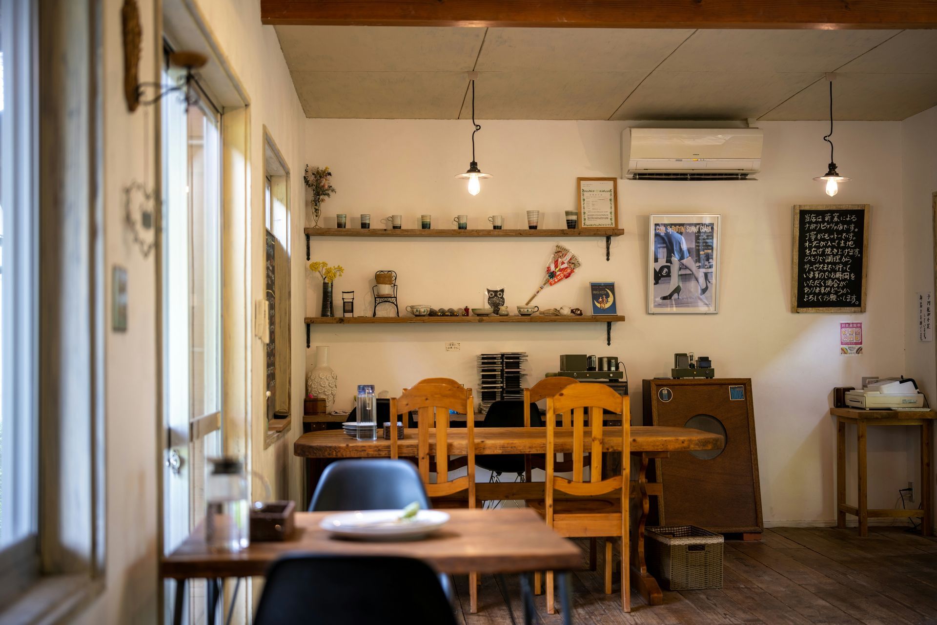 Cozy cafe interior with wooden tables and chairs, shelves of items, and hanging lights.