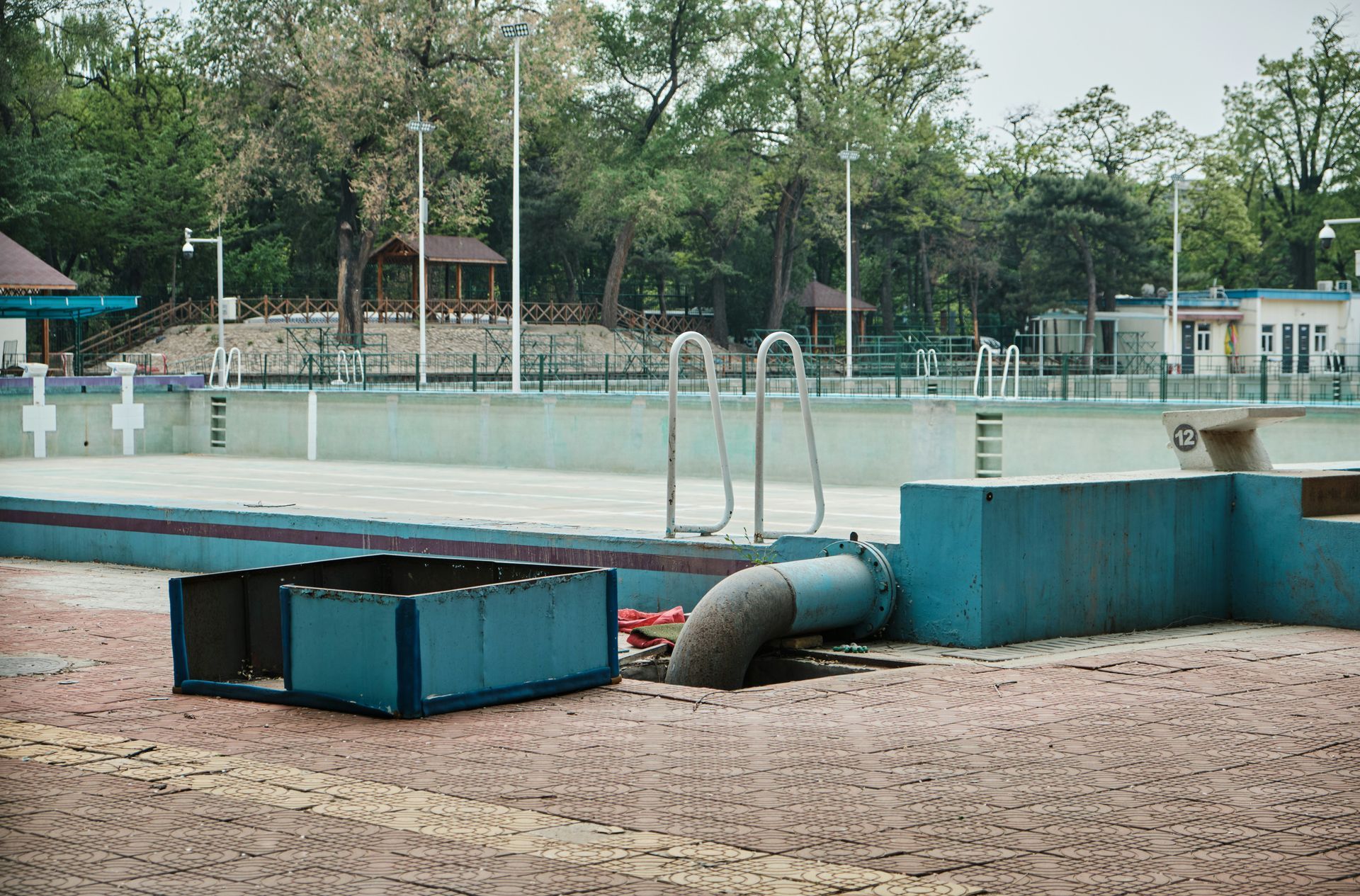 Empty blue swimming pool; outdoor setting with trees and a pipe discharging sediment.