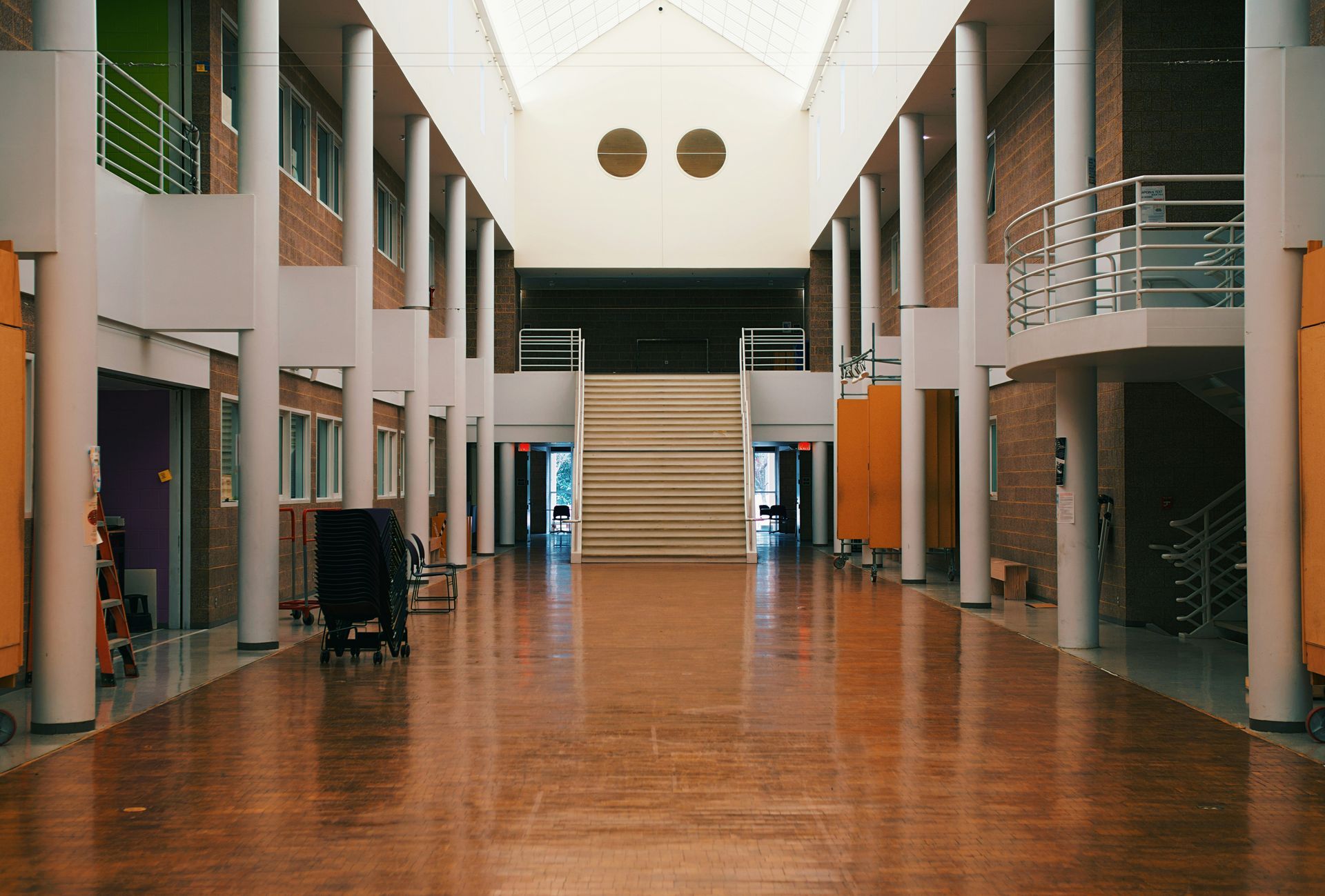 Long hallway in a building with wooden floors, brick walls, and white pillars. Staircase at end.