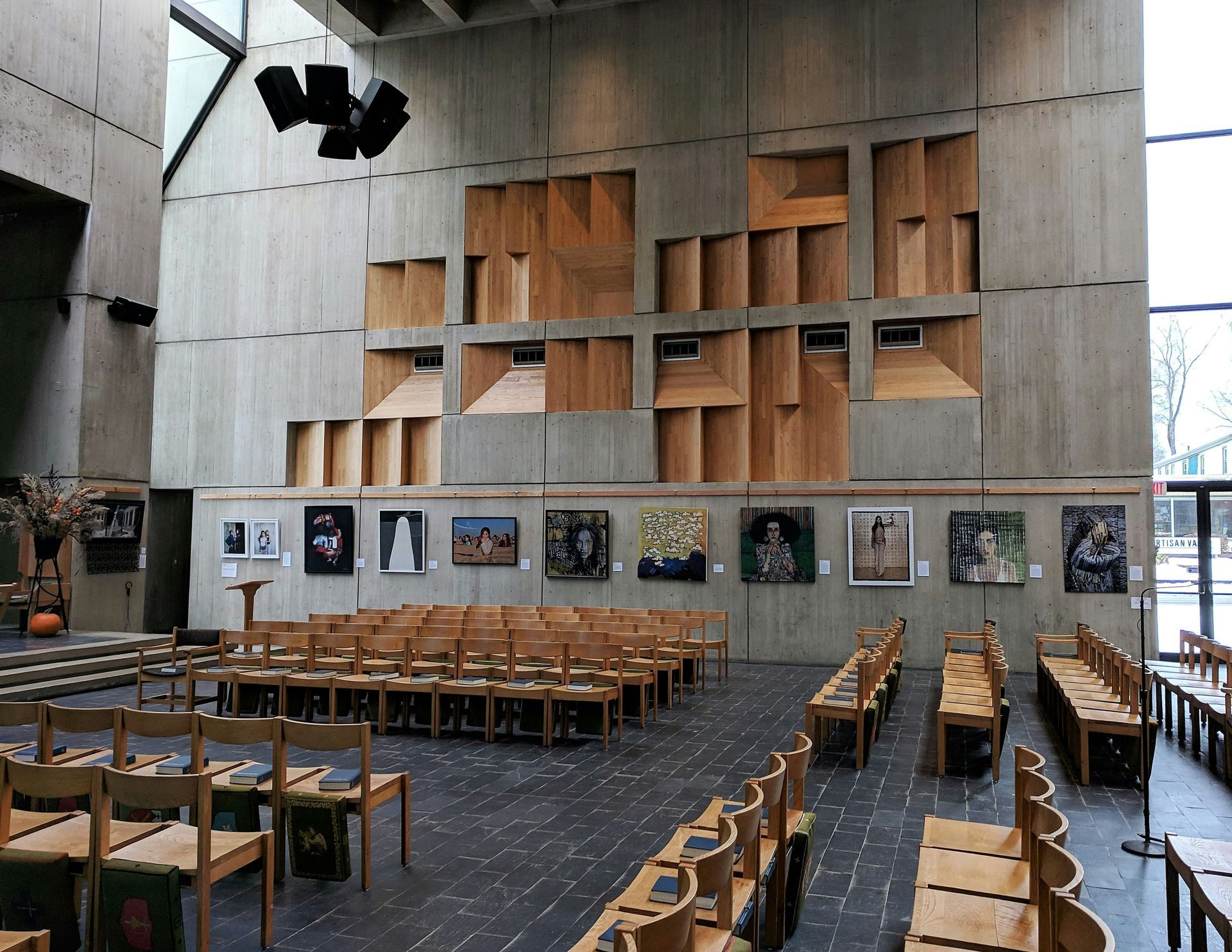 An interior of a church with wooden pews, artwork, and a concrete wall featuring wooden cubbies.
