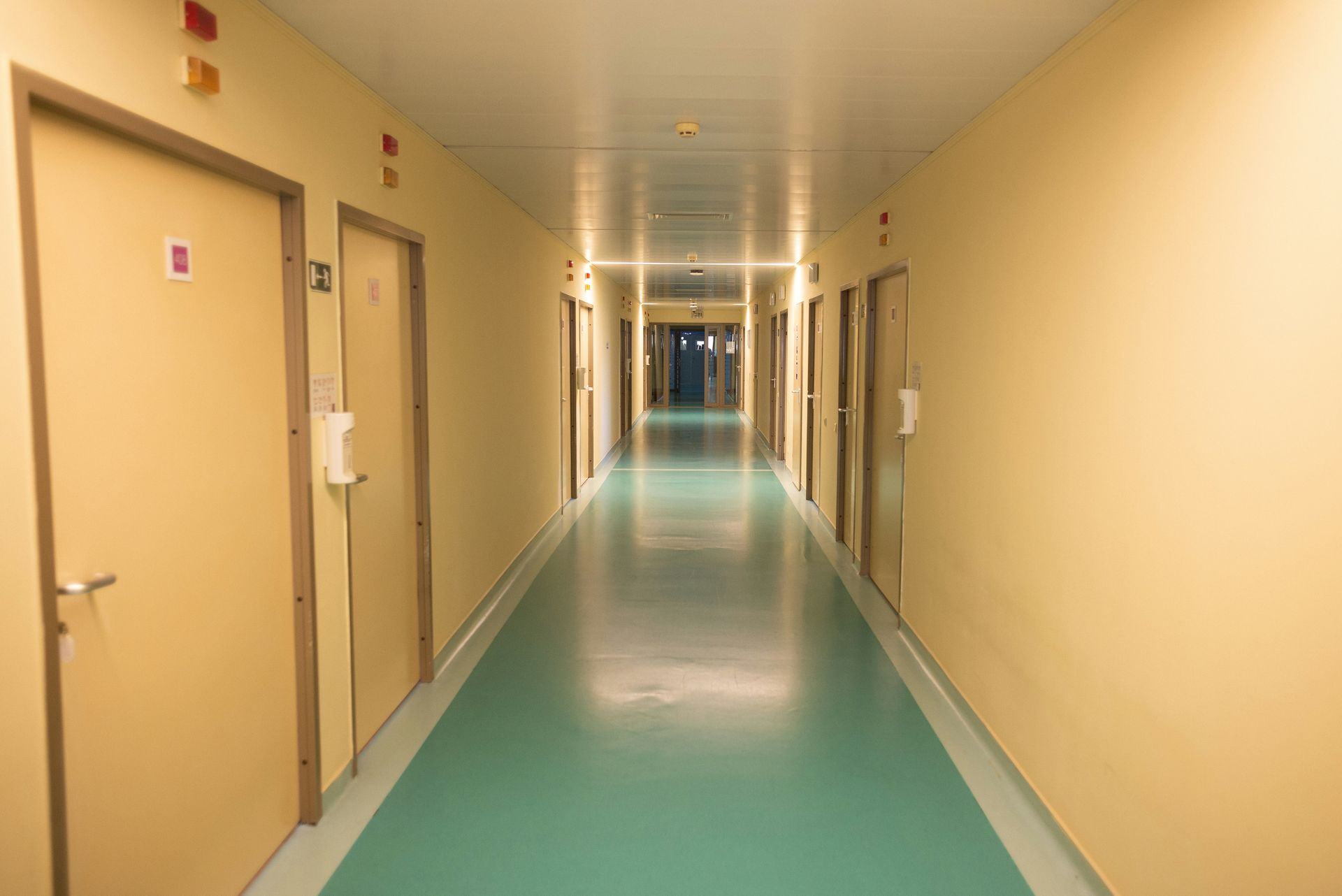 Long, empty hallway with beige doors and teal floor.