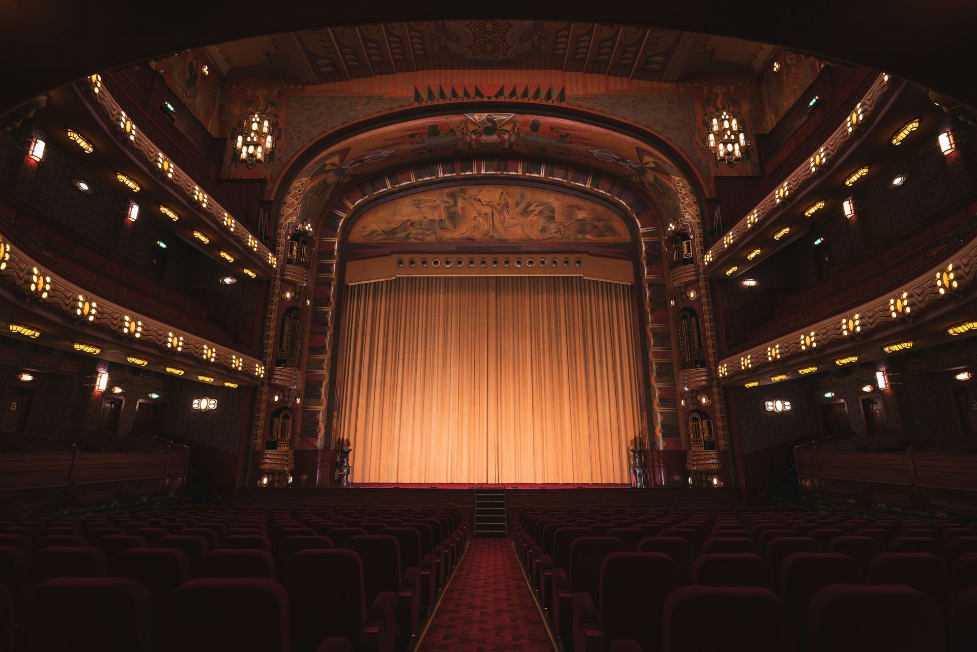 Empty ornate theater with red seating and closed stage curtain.