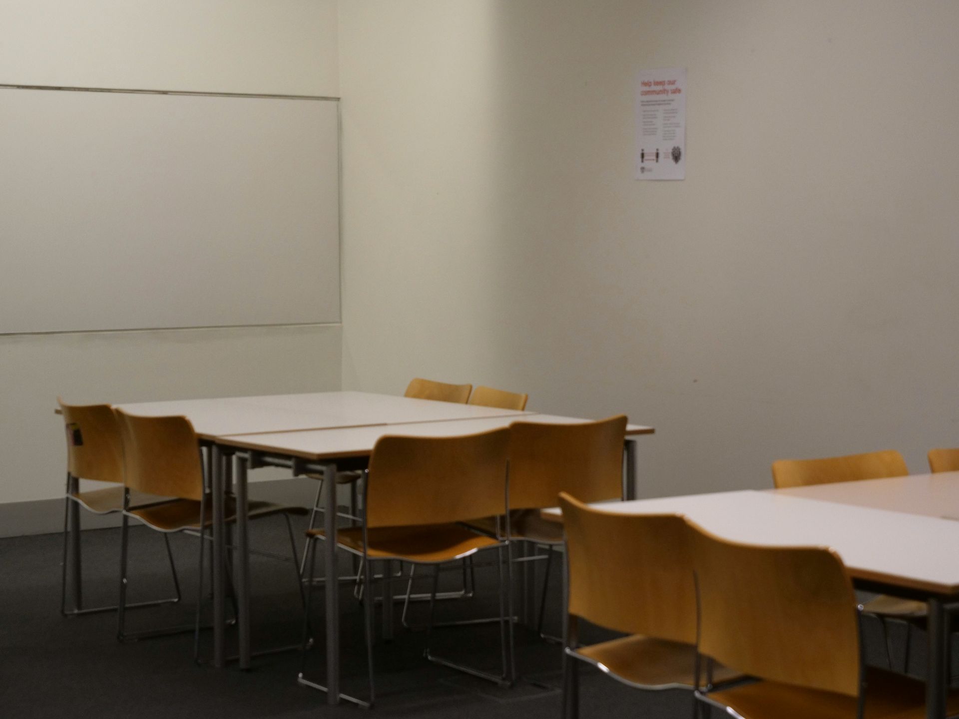 Empty classroom with tables, chairs, whiteboard, and a poster on the wall.