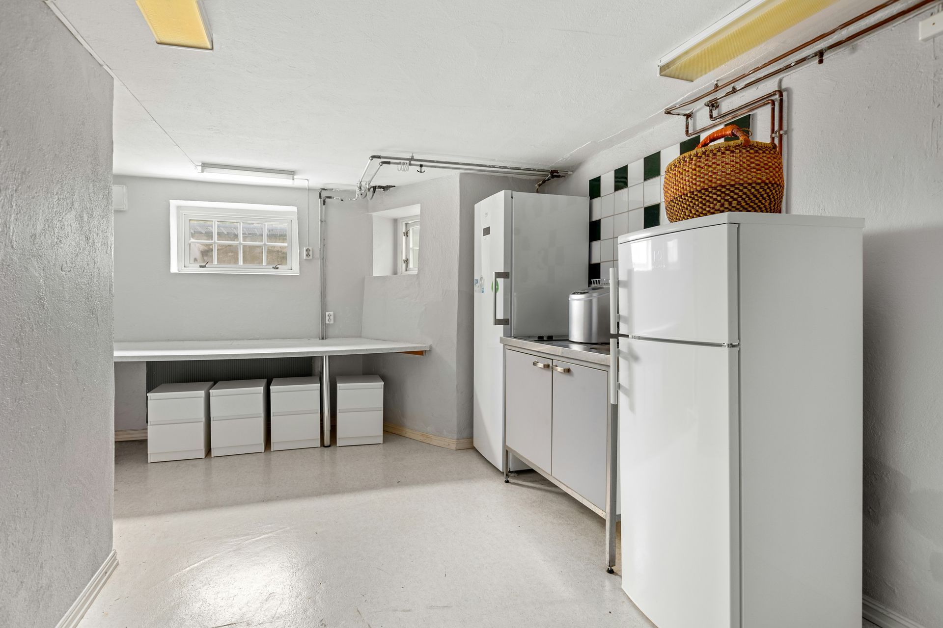 Basement with white appliances, cabinets, and a long counter. A wicker basket sits atop a fridge.
