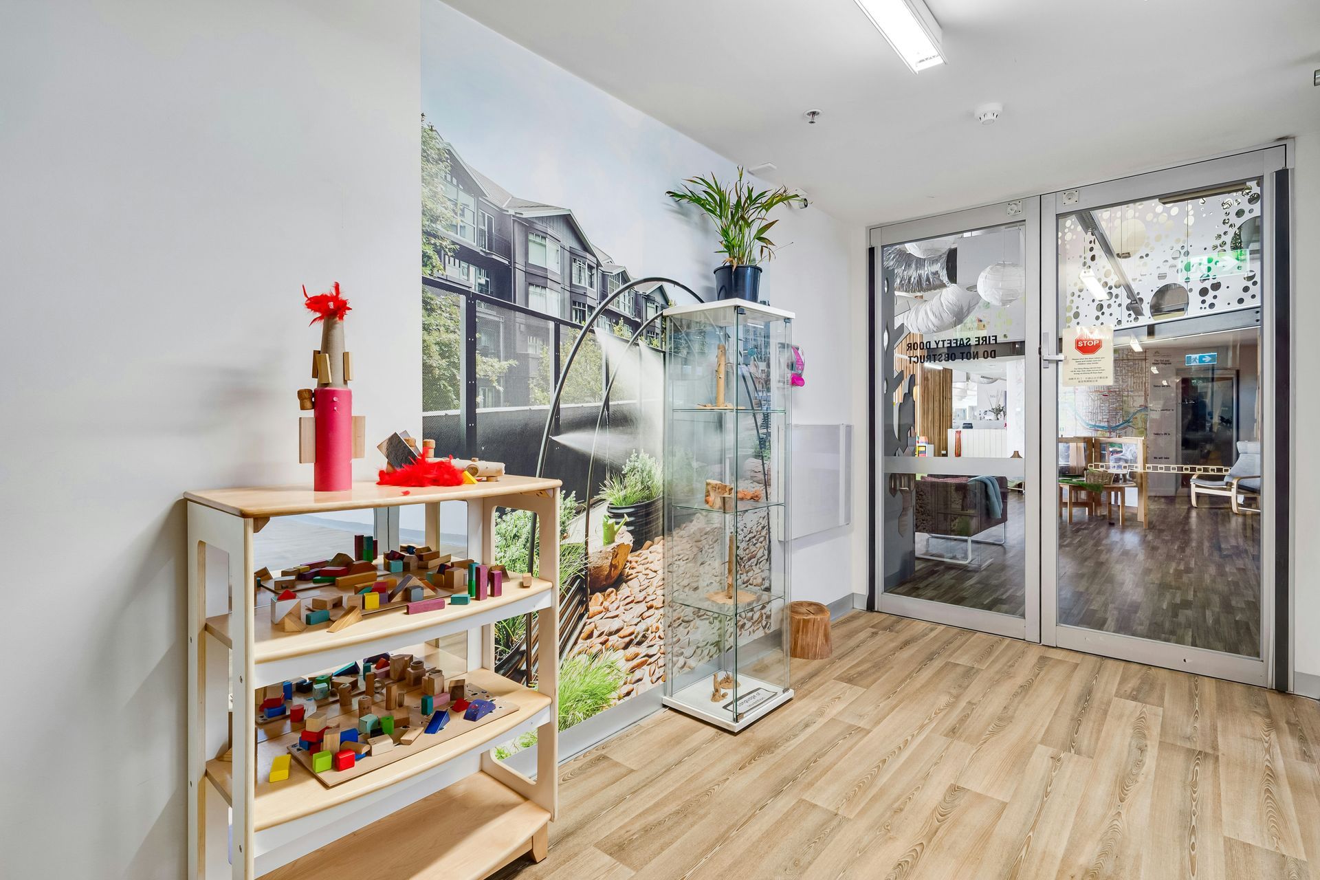 A child's playroom hallway with wooden shelves of toys and glass doors to another room.