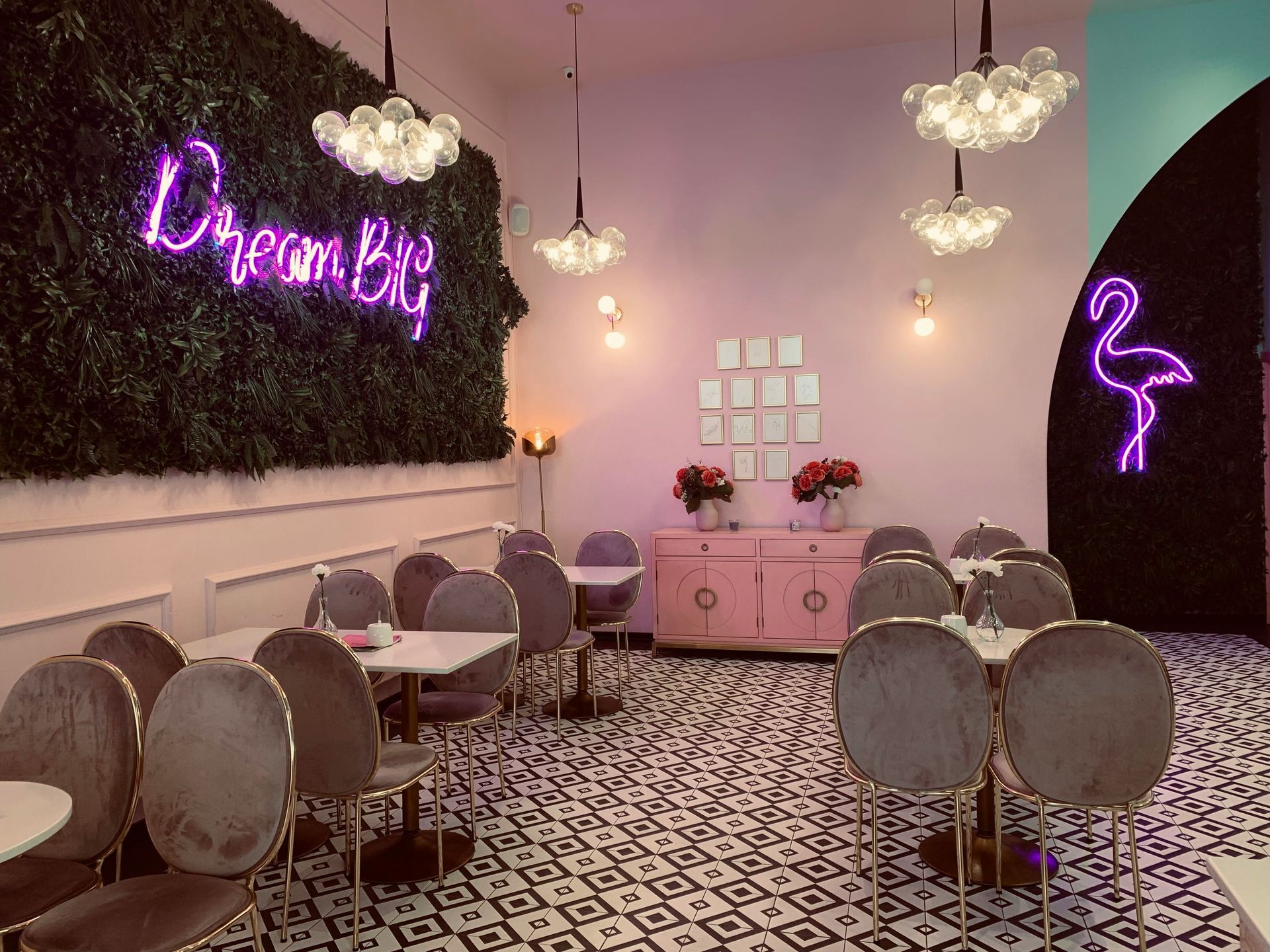Cafe interior with tables, velvet chairs, floral accents, and neon signs, including 
