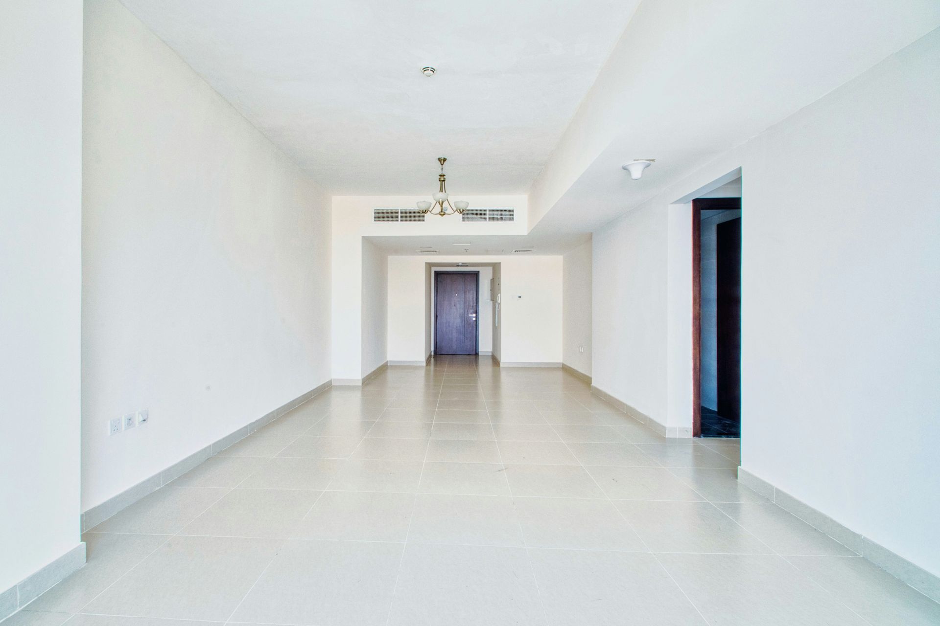 Empty white-walled room with a tile floor, doorway, and light fixture.