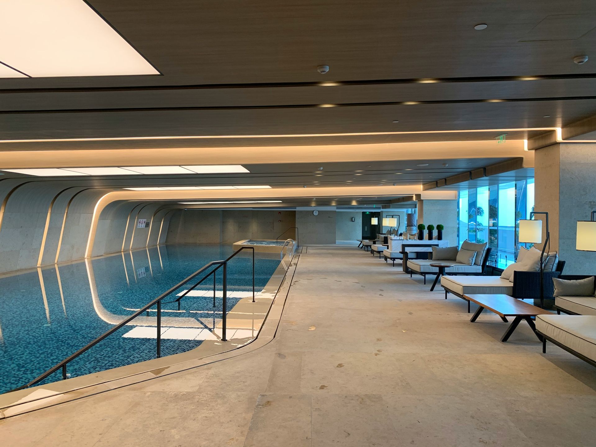 Indoor swimming pool with lounge area, blue water, neutral tones, and modern design.