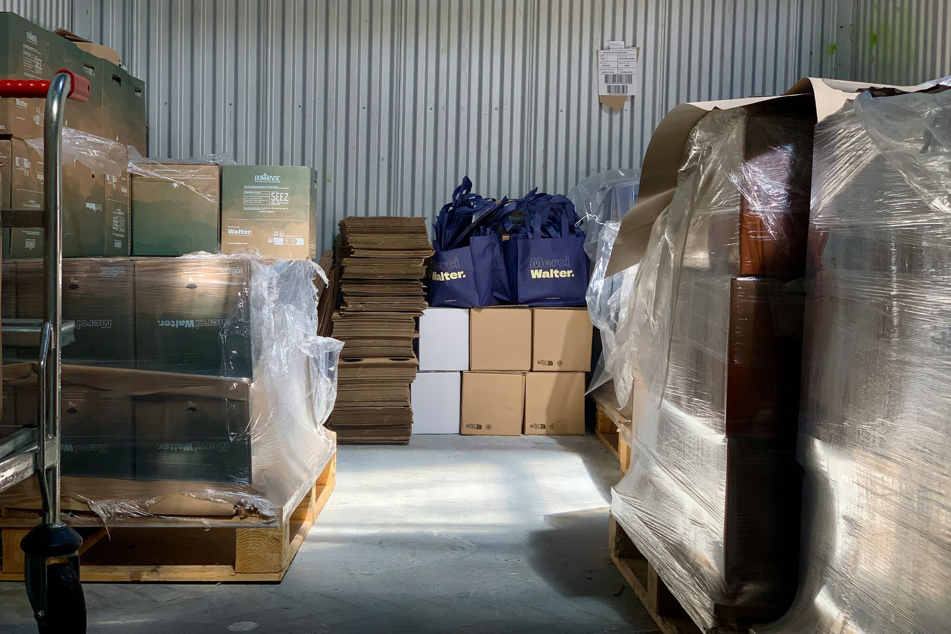 Warehouse interior with stacked pallets of boxes, plastic wrap, and blue bags.