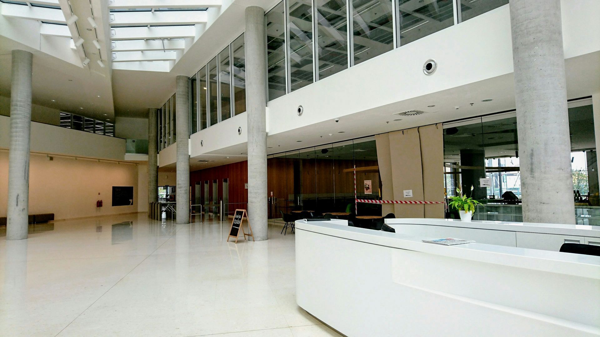 Spacious, white-tiled lobby with large windows and support columns. A white reception desk is in the foreground.