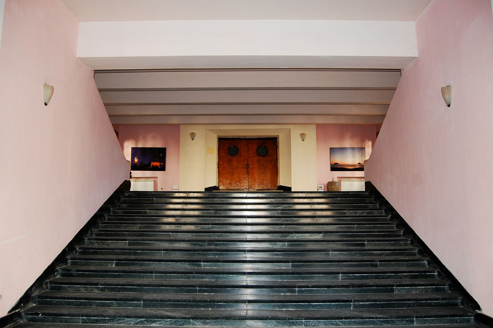Pink walls frame a black marble staircase leading to wooden double doors.