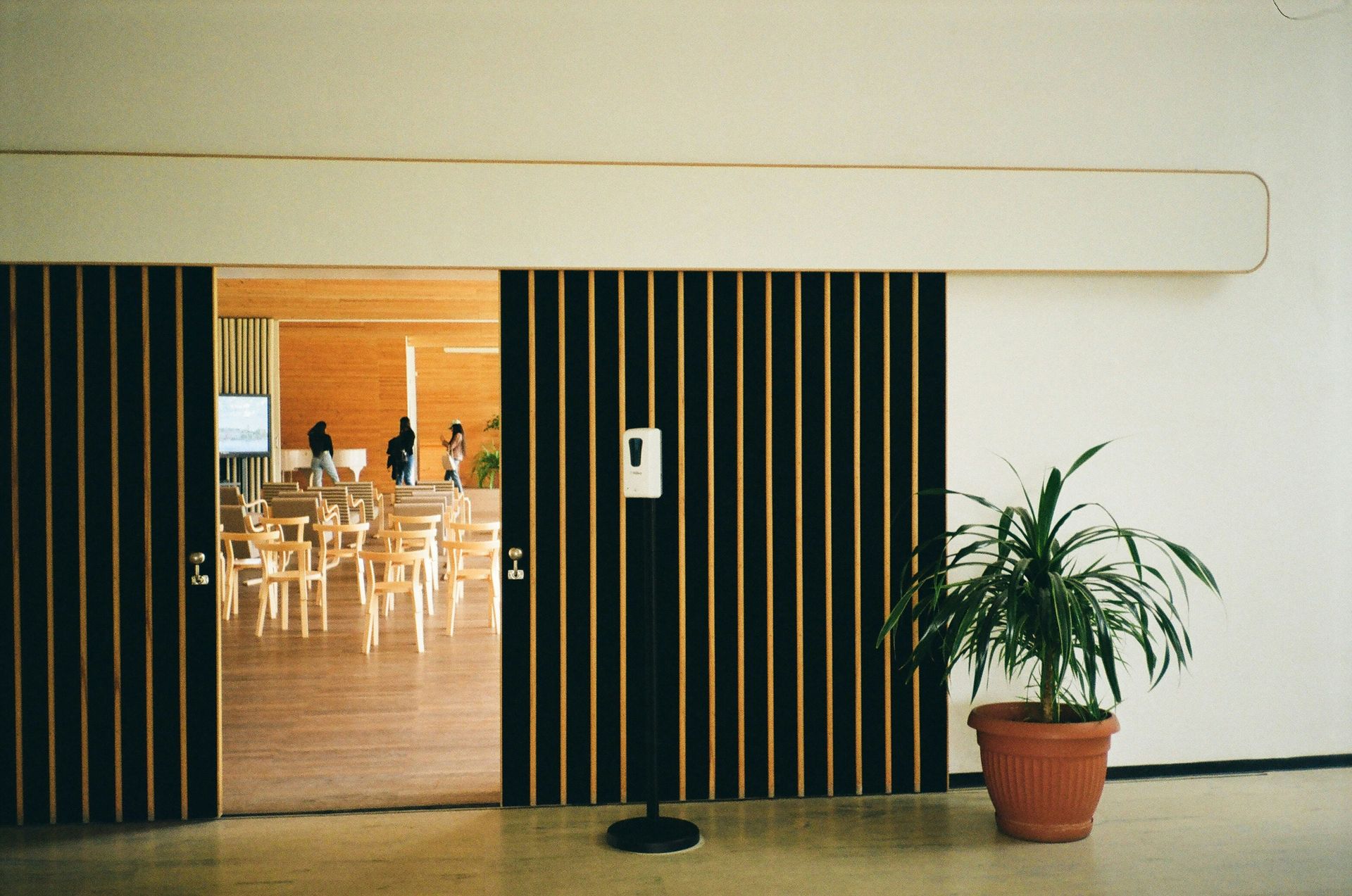 Sliding wood slat doors open to a brightly lit room with tables and chairs; a plant sits beside the doors.