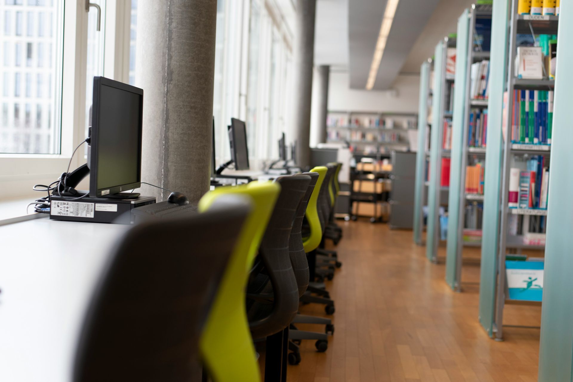 Library computer workstation with chairs, bookshelves, and large windows.