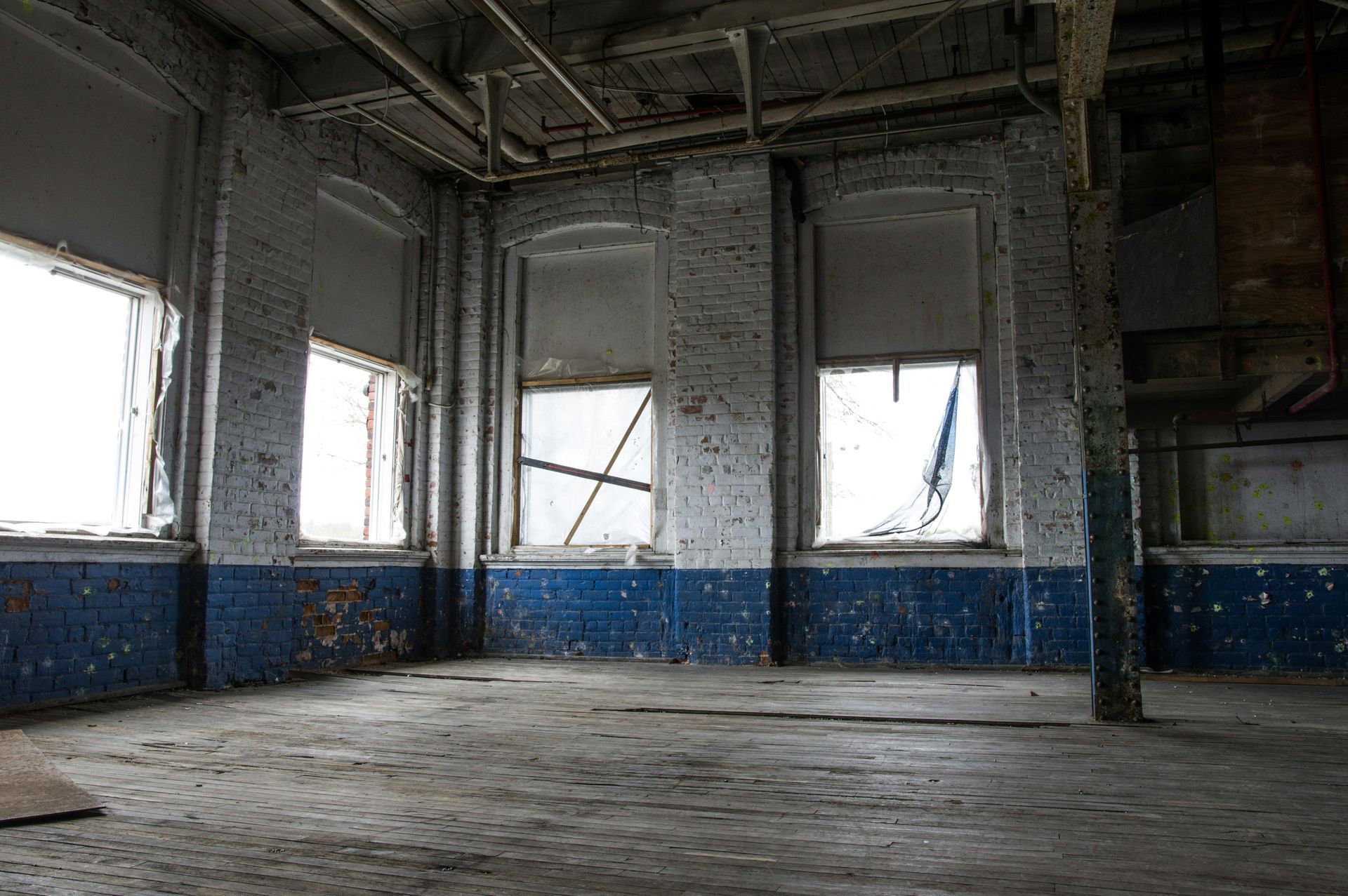 Abandoned room interior with peeling blue paint, broken windows, and debris-covered floor.