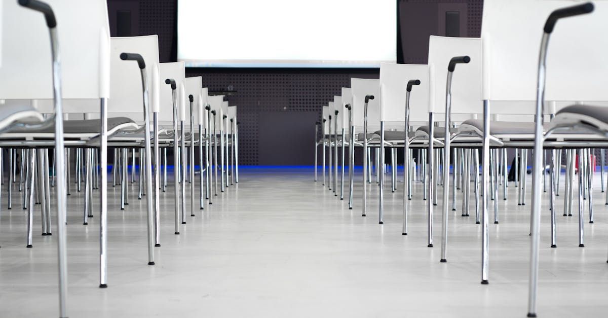 Rows of empty chairs and tables in a classroom, leading to a screen at the front.