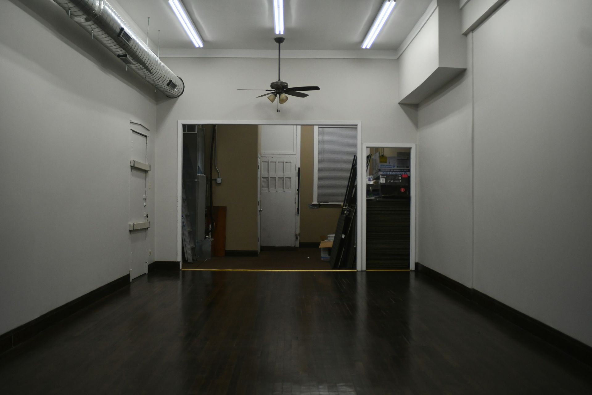 Empty room with dark wood floor and white walls. A doorway leads to another room. Fluorescent lights.