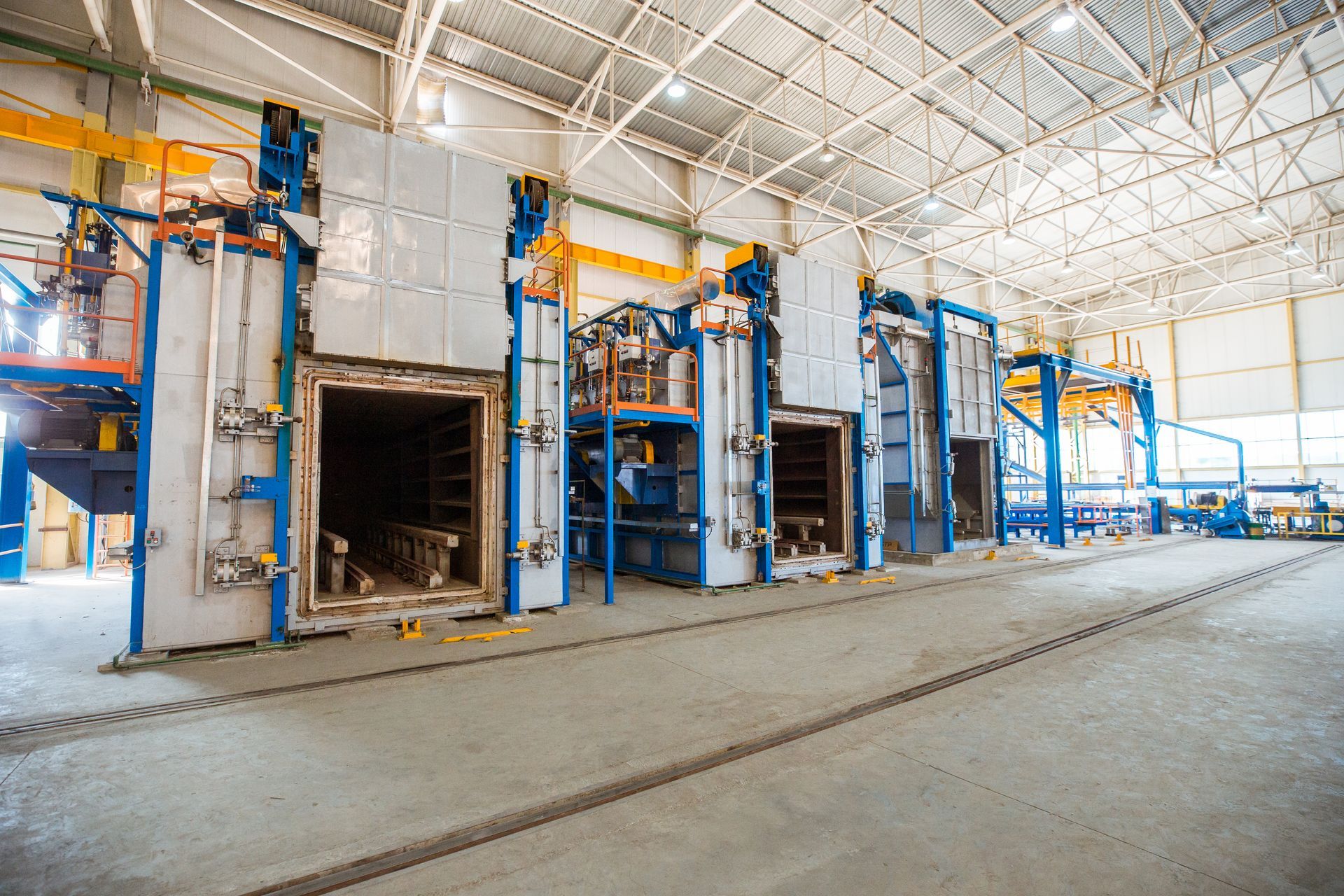 Large industrial ovens inside a factory with bright lights and a concrete floor.