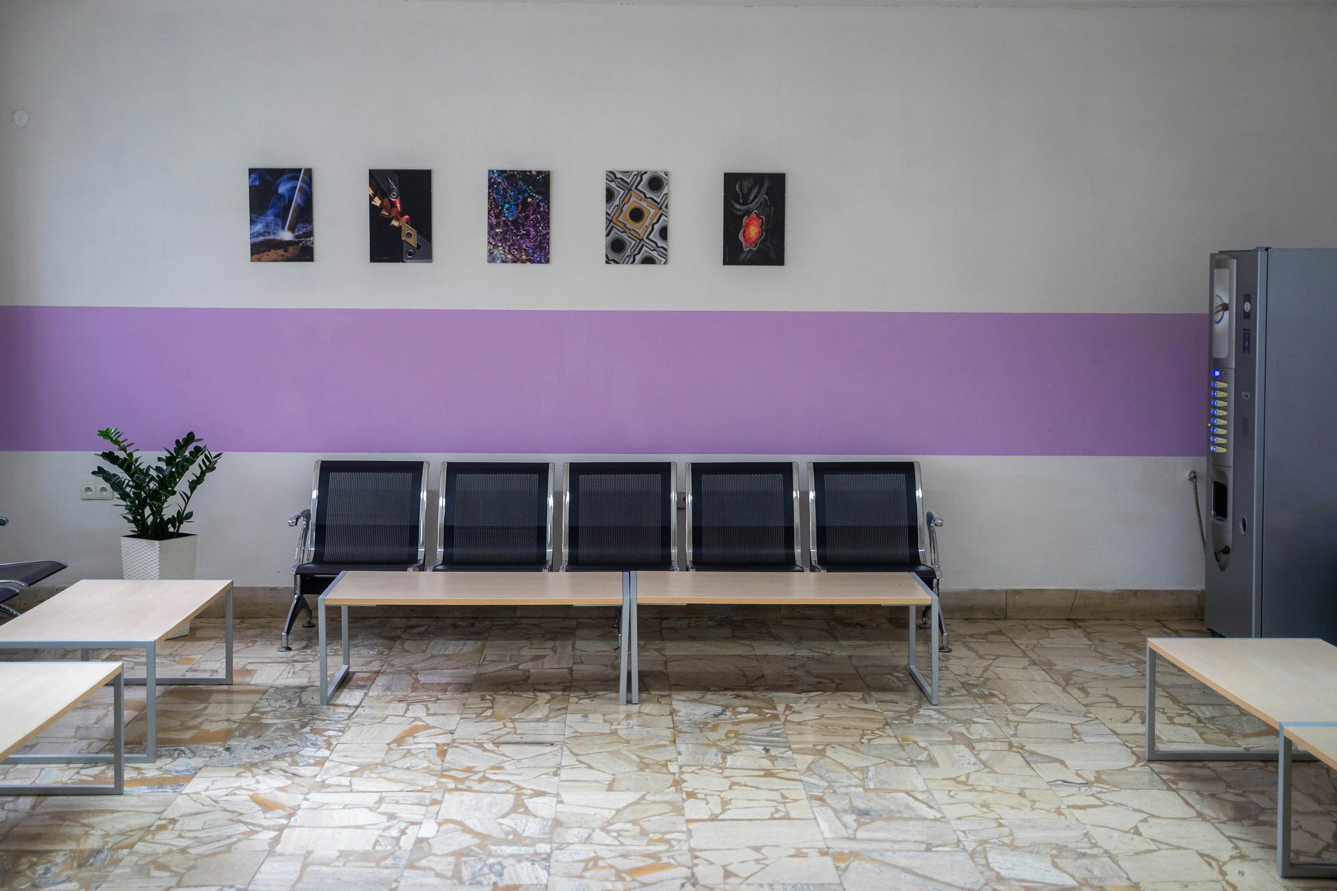 Waiting room with six black mesh chairs, artwork, and purple wall stripe.