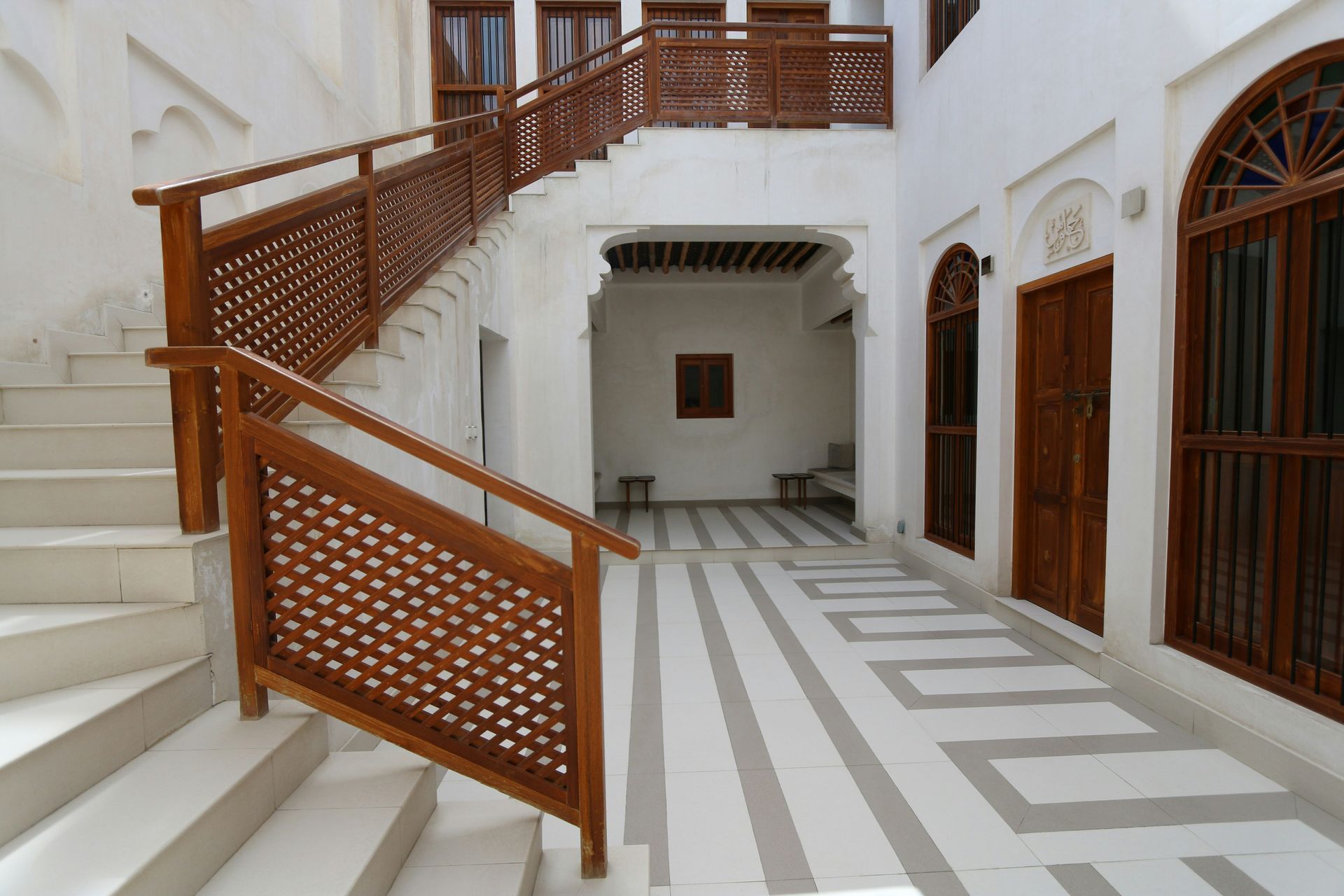 Courtyard with staircase, white walls, wood railings and windows, patterned floor.