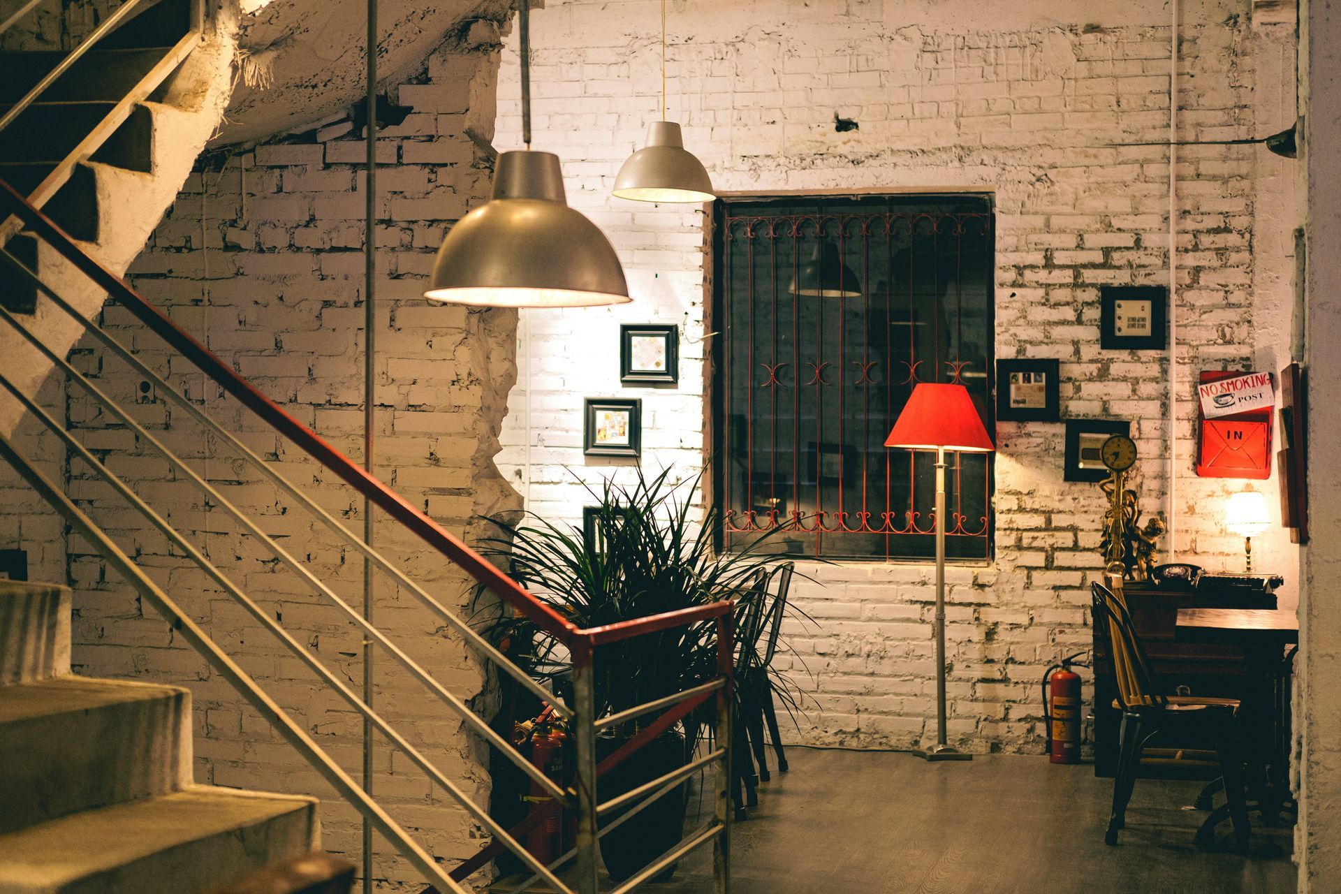 Interior with stairs, white brick wall, metal railings, pendant lights, framed artwork, and a red floor lamp.