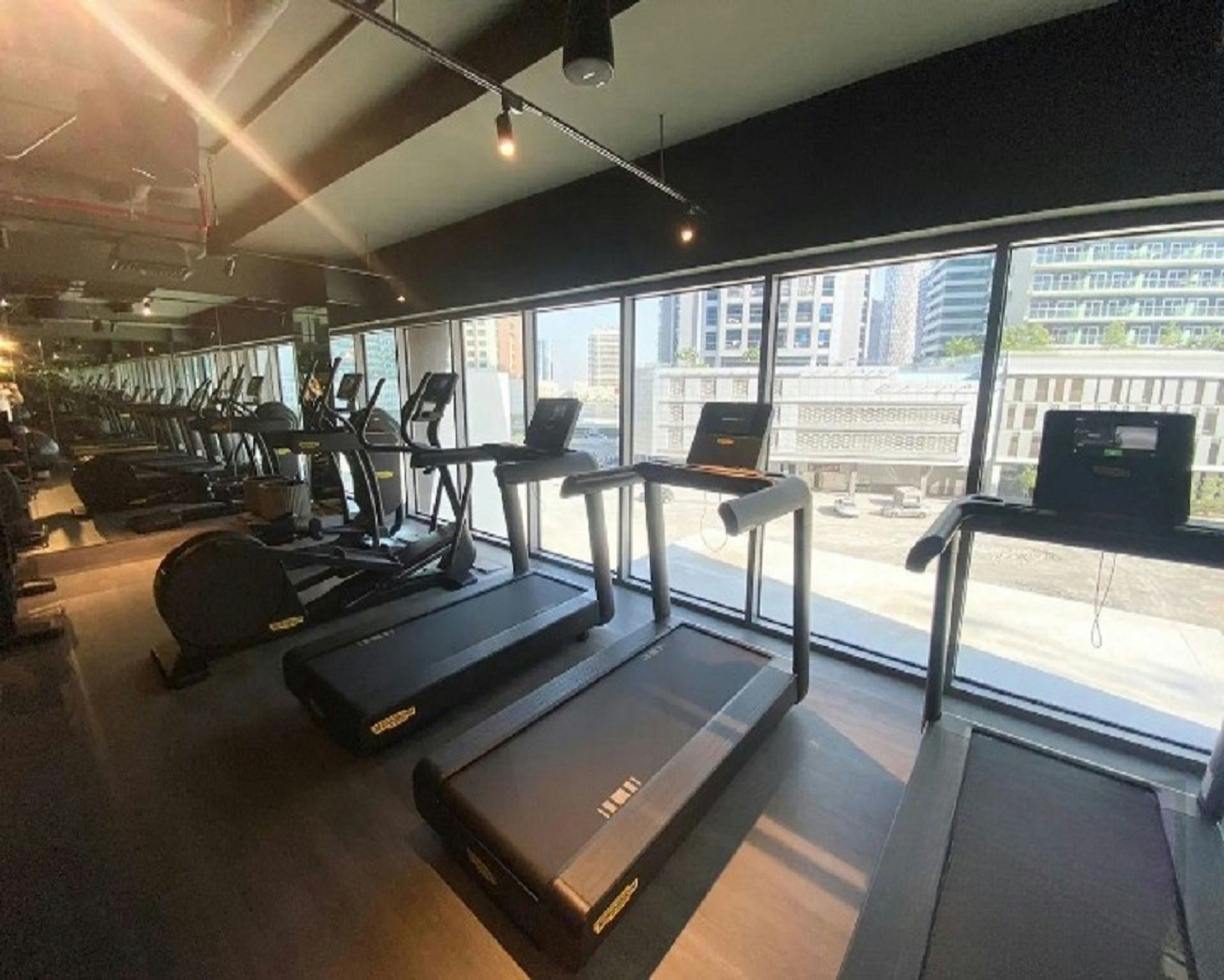 Gym with treadmills and elliptical machines by a large window overlooking a city.