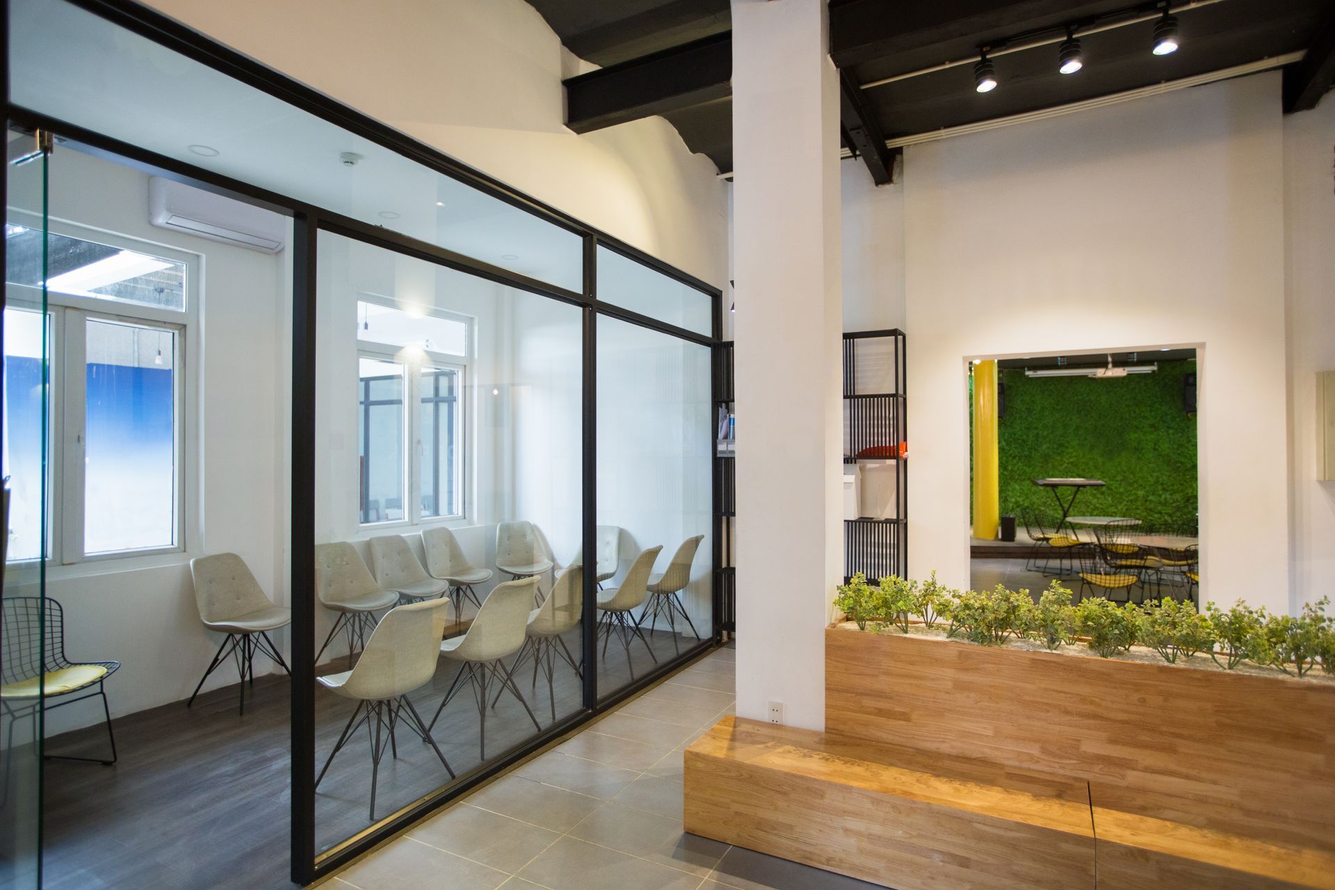 A modern office interior featuring a glass-walled conference room with several white chairs and a wooden planter in front.