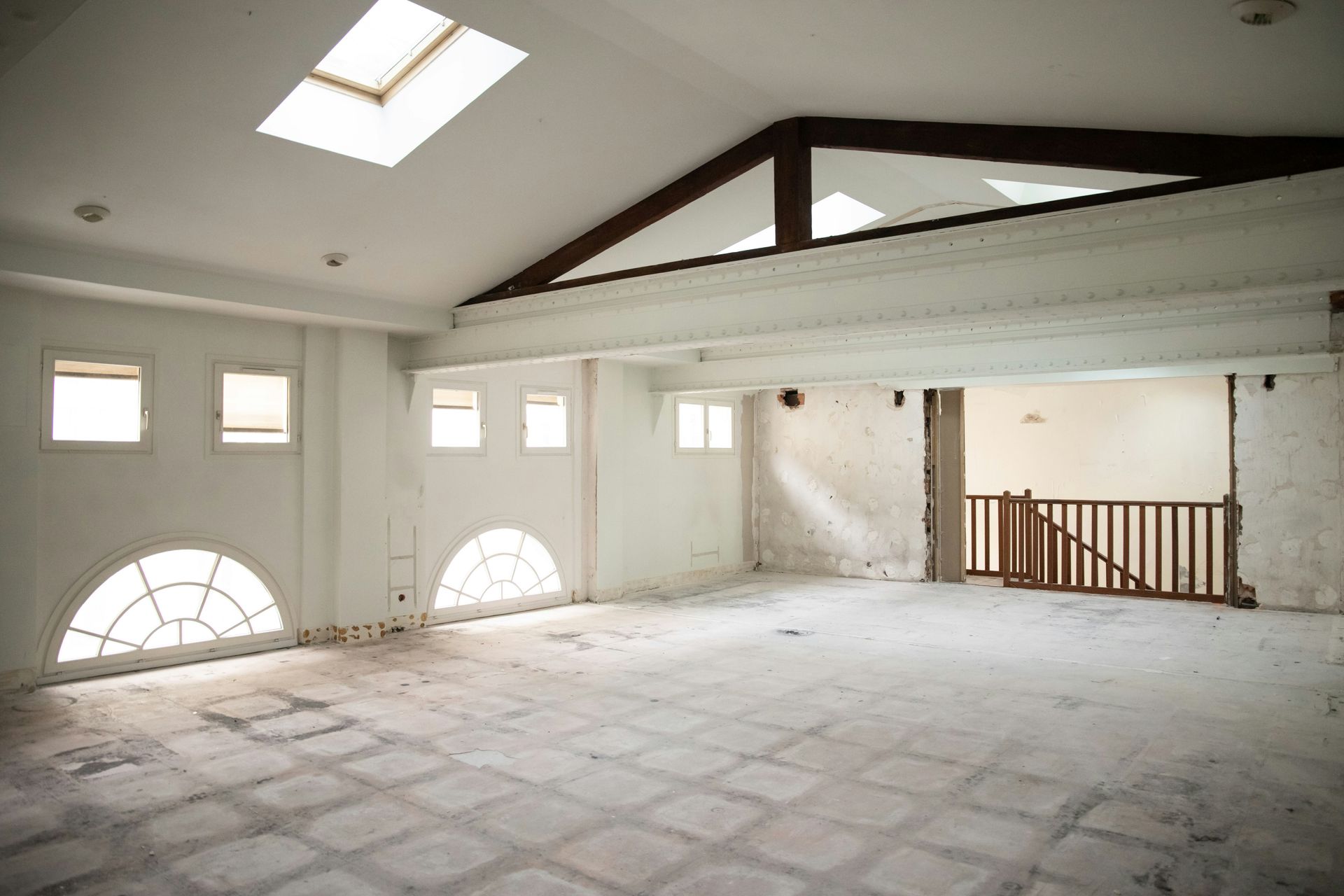 Empty, white-walled room with vaulted ceiling, arched windows, and a raised section with a staircase.