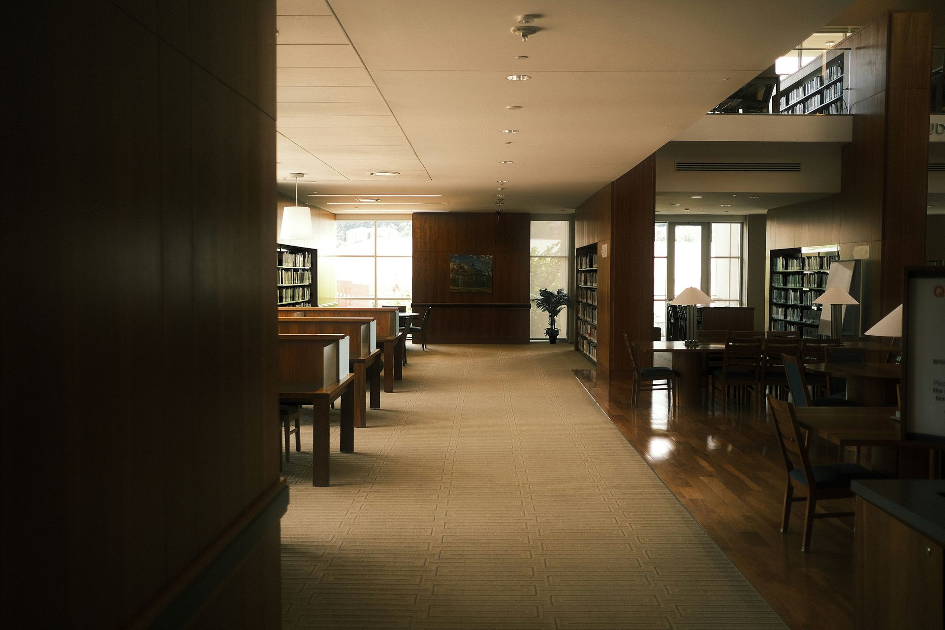 Library interior with bookshelves, tables, and a long hallway with natural light.