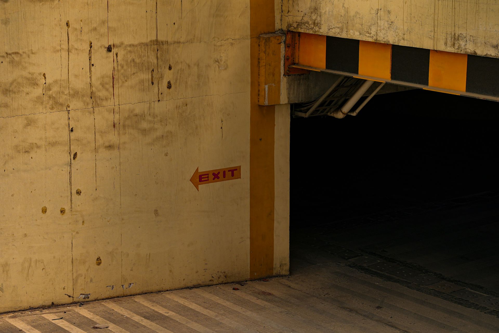 Concrete parking garage exit with yellow and black striped overhead beam; exit sign.