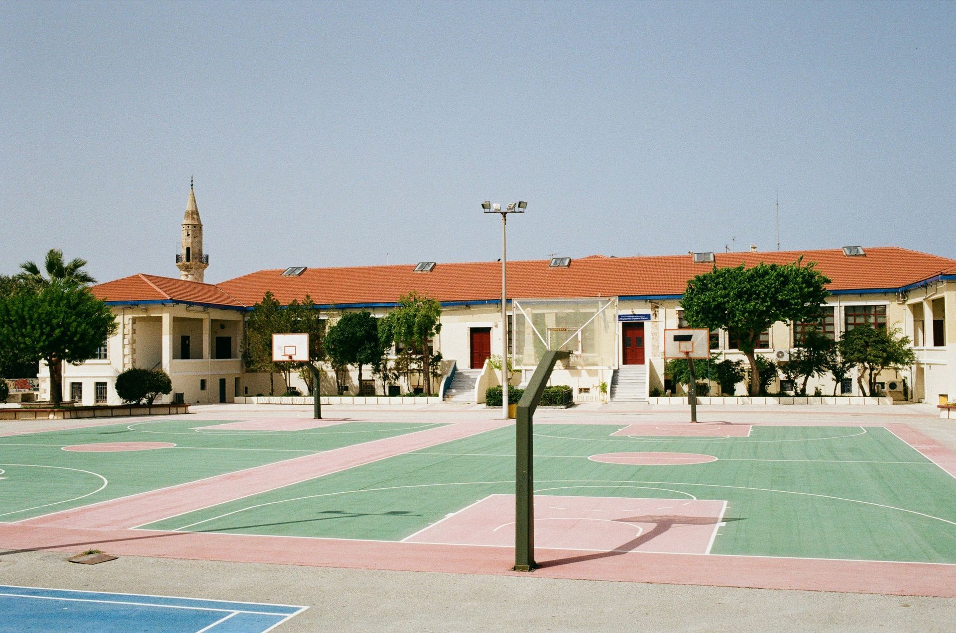 Schoolyard with basketball courts, red-roofed building, and a minaret.
